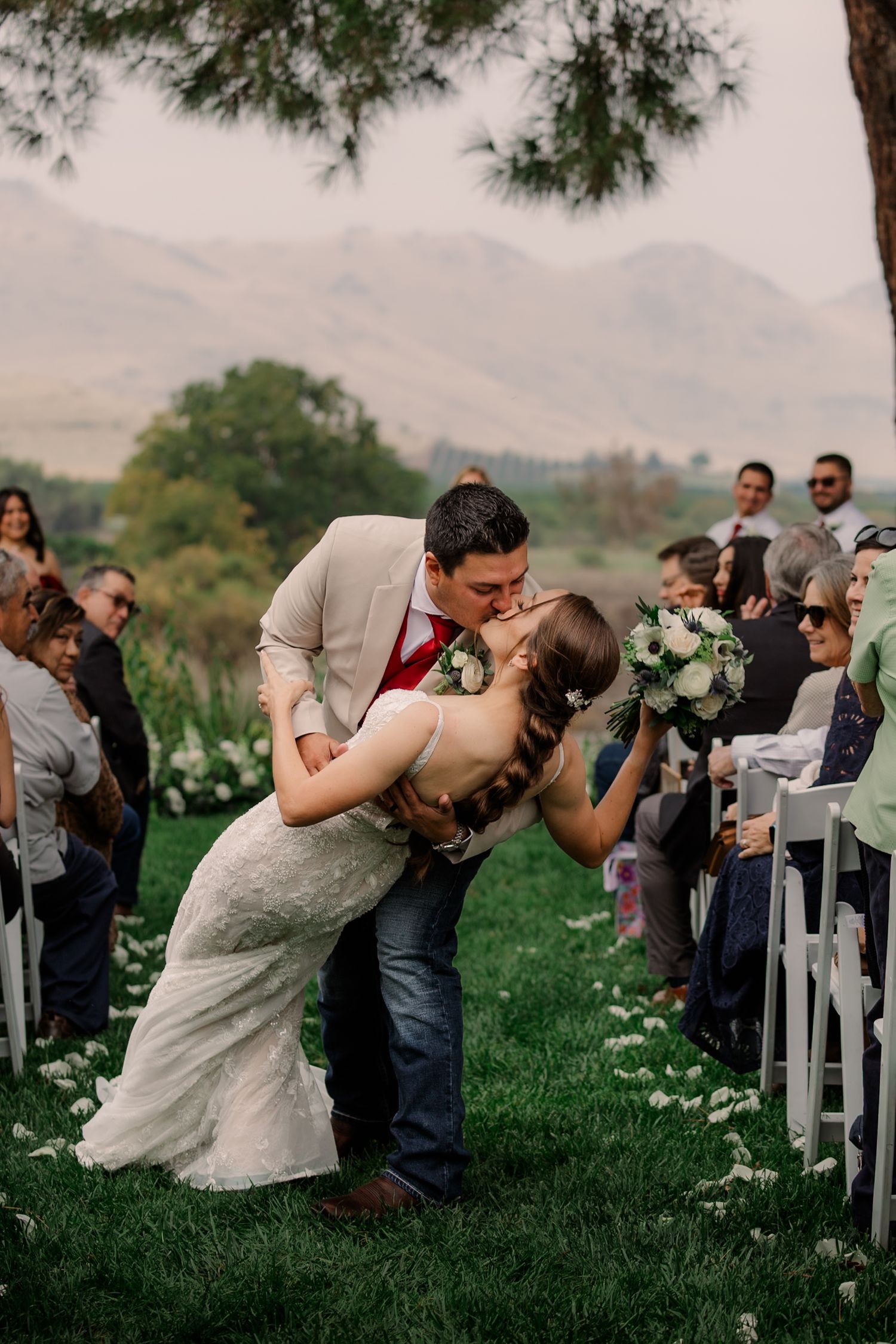 Wedding ceremony guests seated on white chairs in a garden setting with mountain views.