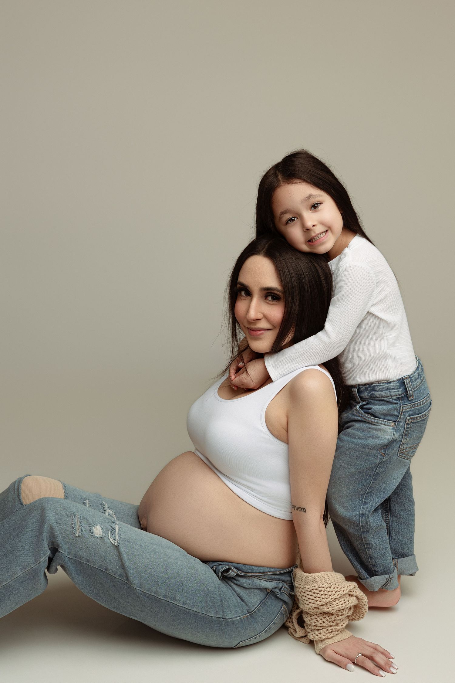 A series of artistic maternity photos showing someone in casual jeans and white top posing against a neutral backdrop.