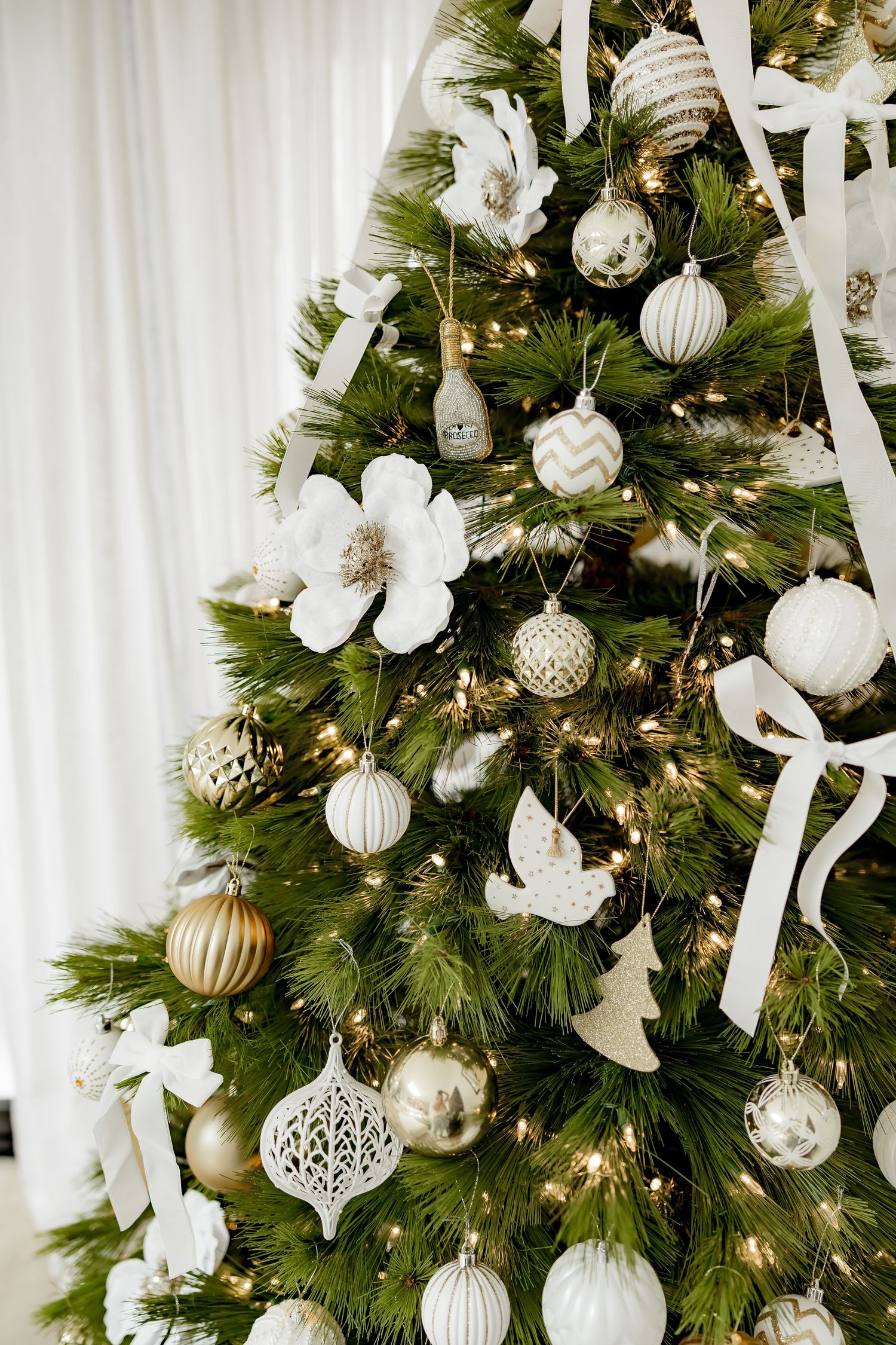 Close-up view of an elegant Christmas tree decorated with white and silver ornaments, ribbons and twinkling lights.