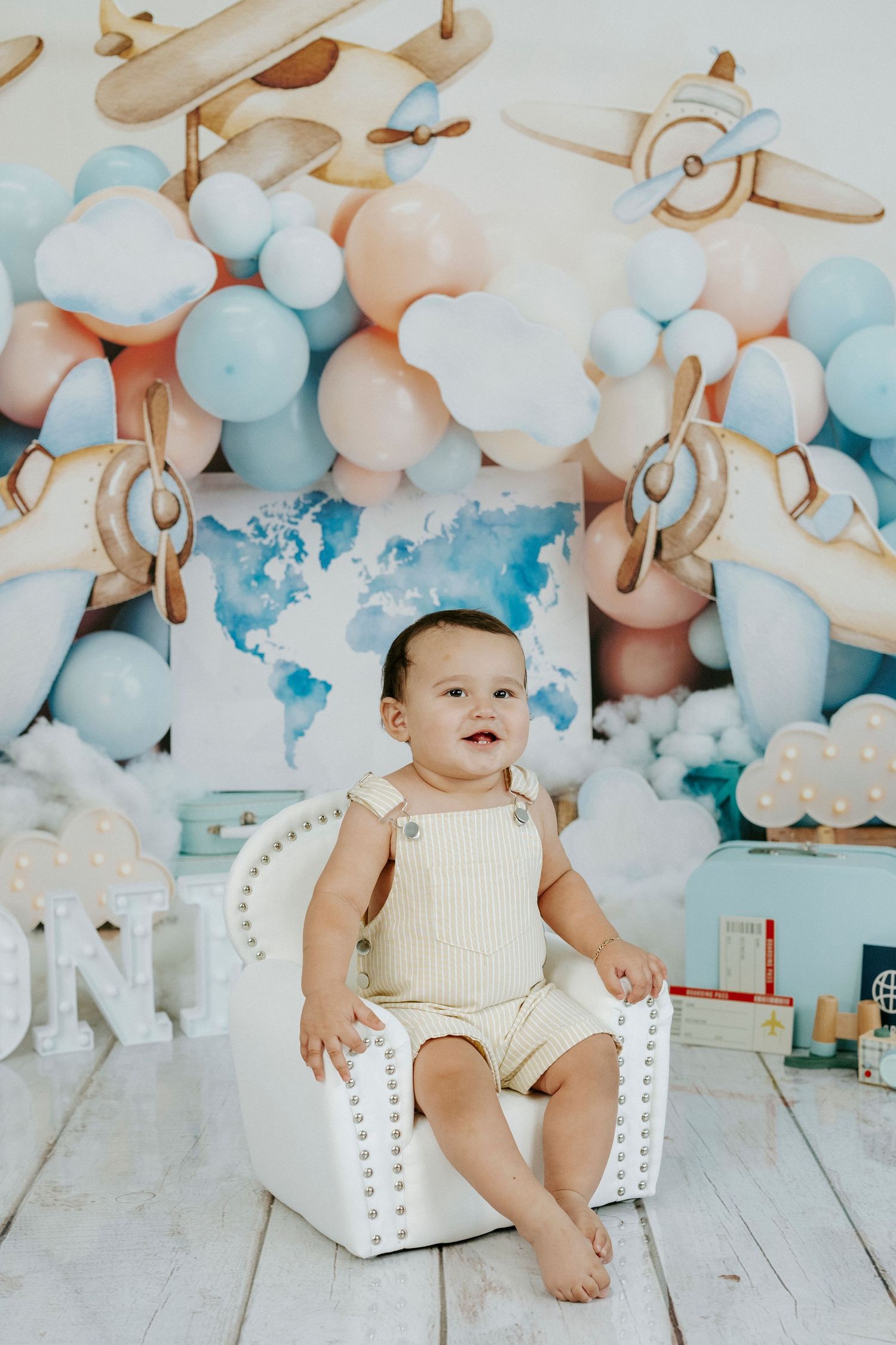 Balloon arch in soft blue and peach tones decorates a white wooden floor with small stuffed animals for a baby photo session.