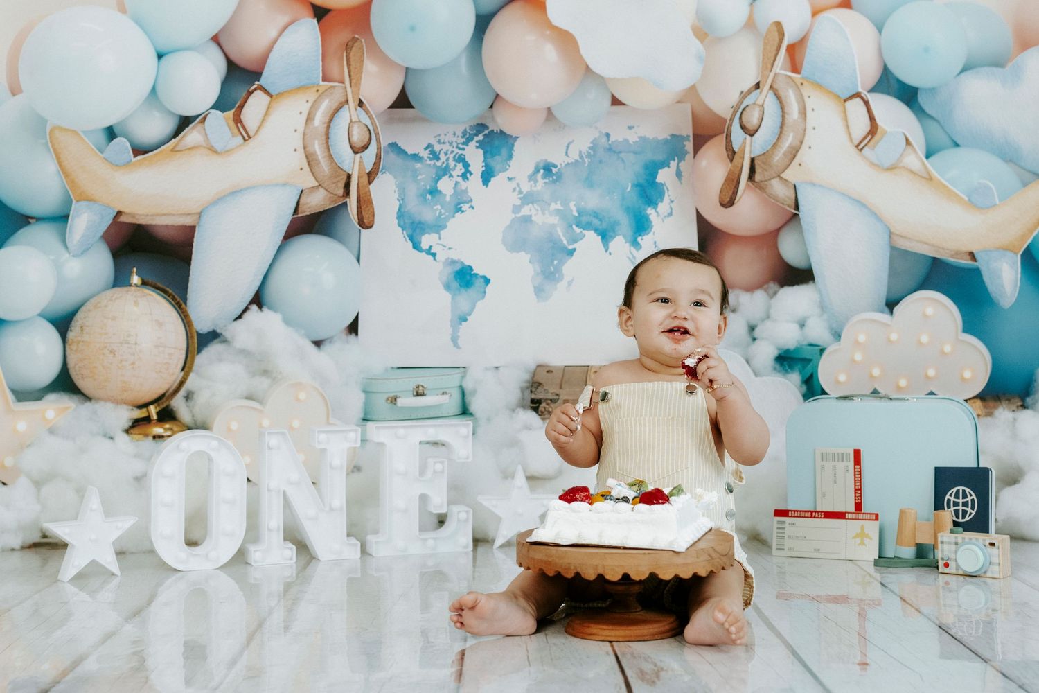 Baby celebrates first birthday with cake smash photo session featuring blue and white balloon decorations and ONE lettering.