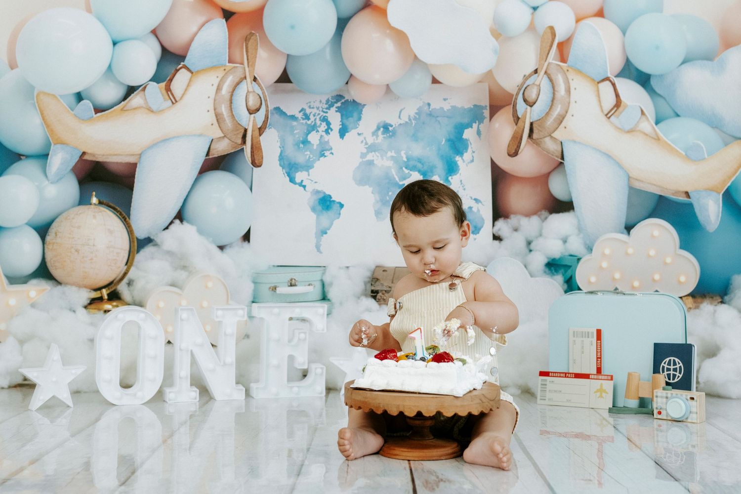 A baby's first birthday cake smash photo session with soft blue and white balloon decorations and teddy bears.