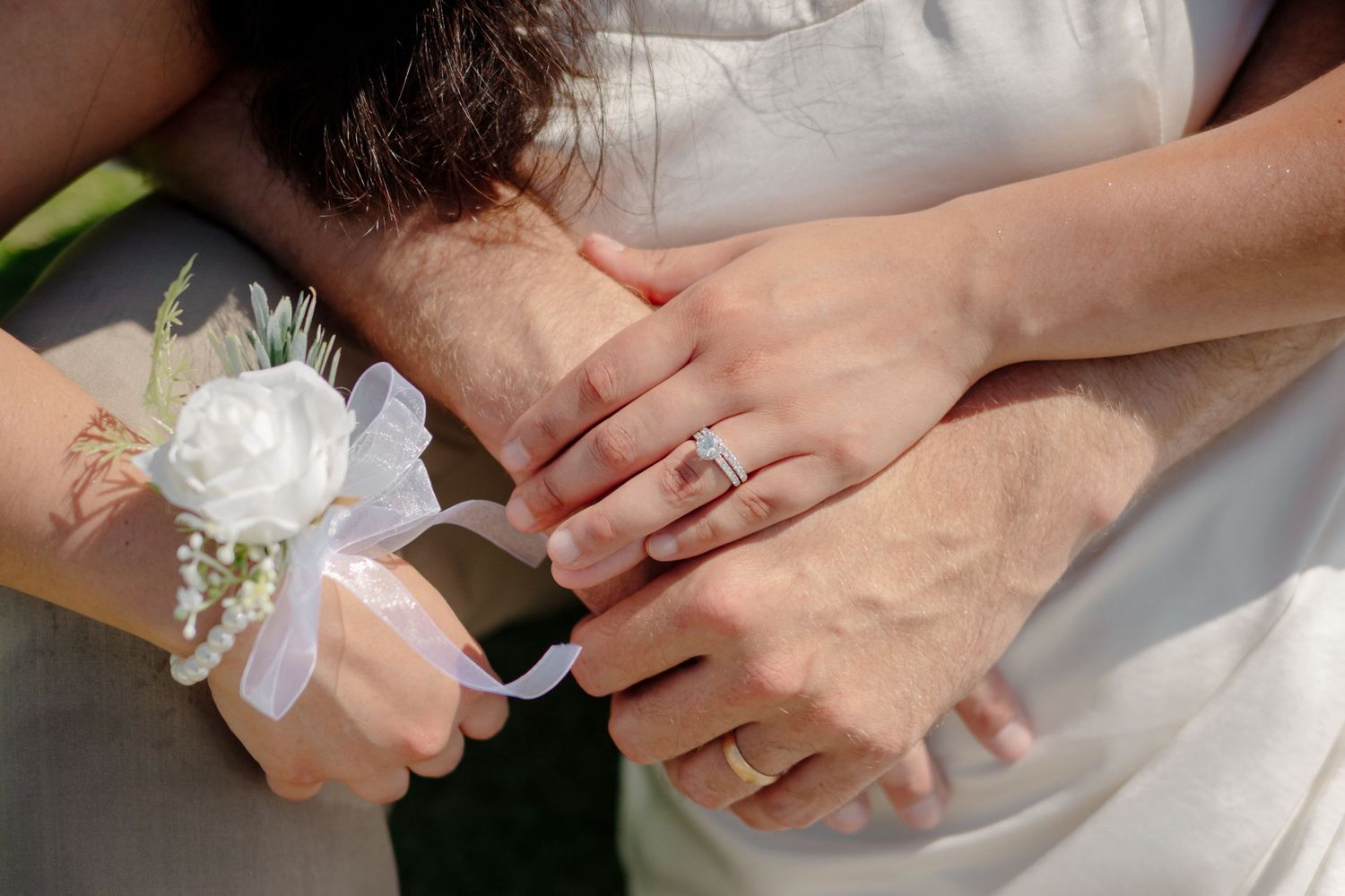 Two hands touching with engagement ring and white corsage wrist flower during wedding ceremony.