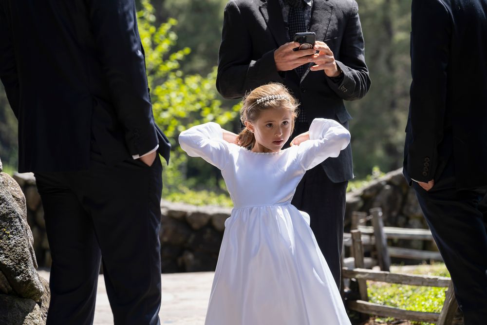 A couple in wedding attire share a candid moment outdoors with trees and greenery in the background.