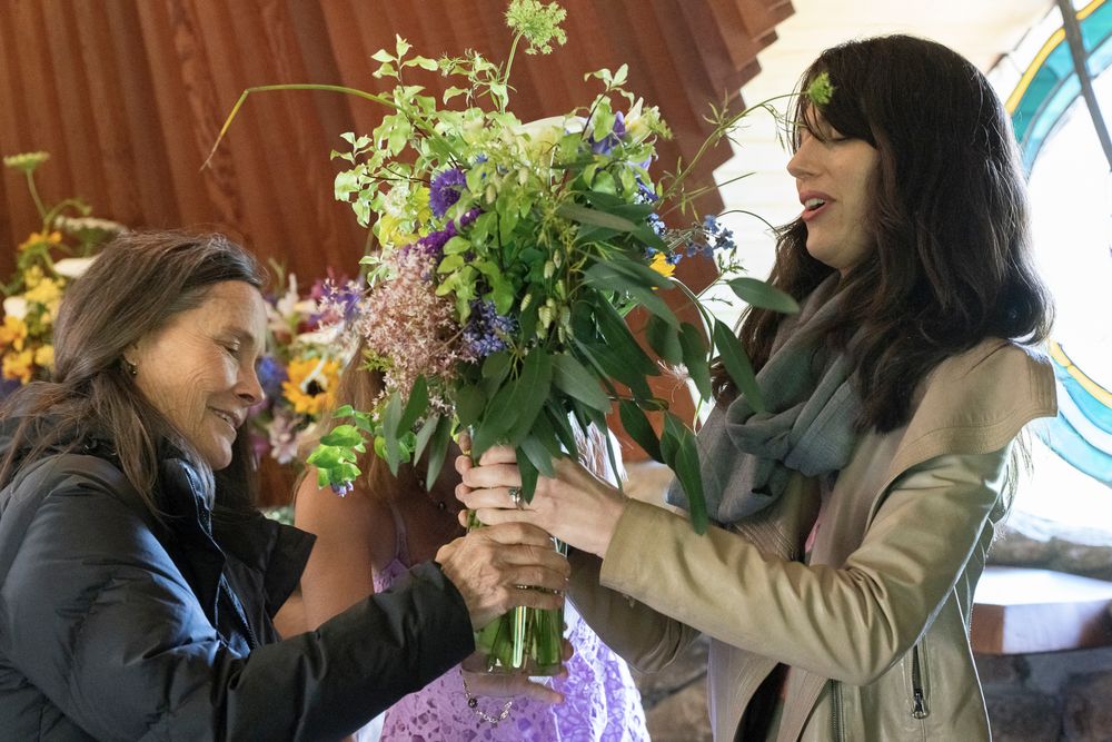 Two people share a joyful moment while arranging a vibrant bouquet of wildflowers indoors.
