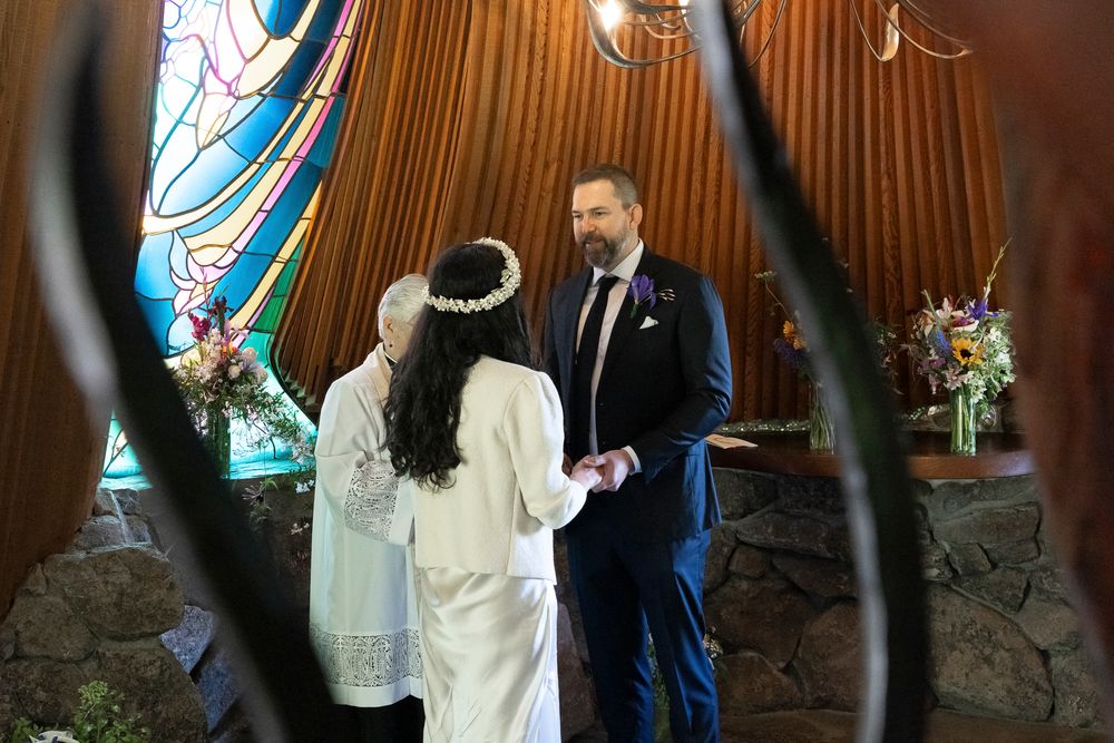 Wedding party members stand in a line against a wood-paneled wall with stained glass windows.