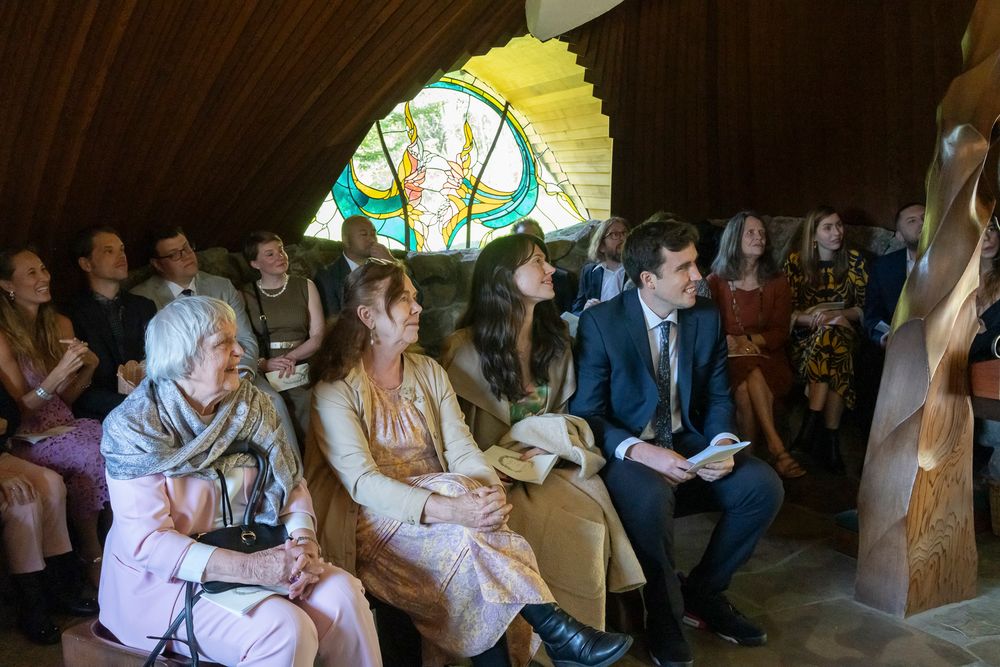 Wedding guests seated in rows beneath a decorative stained glass window during a ceremony.