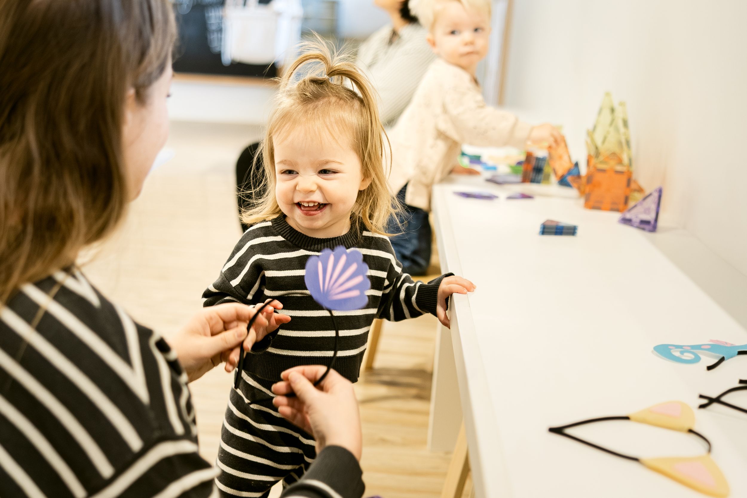 A young child in a striped shirt plays with toys and craft supplies at a table.