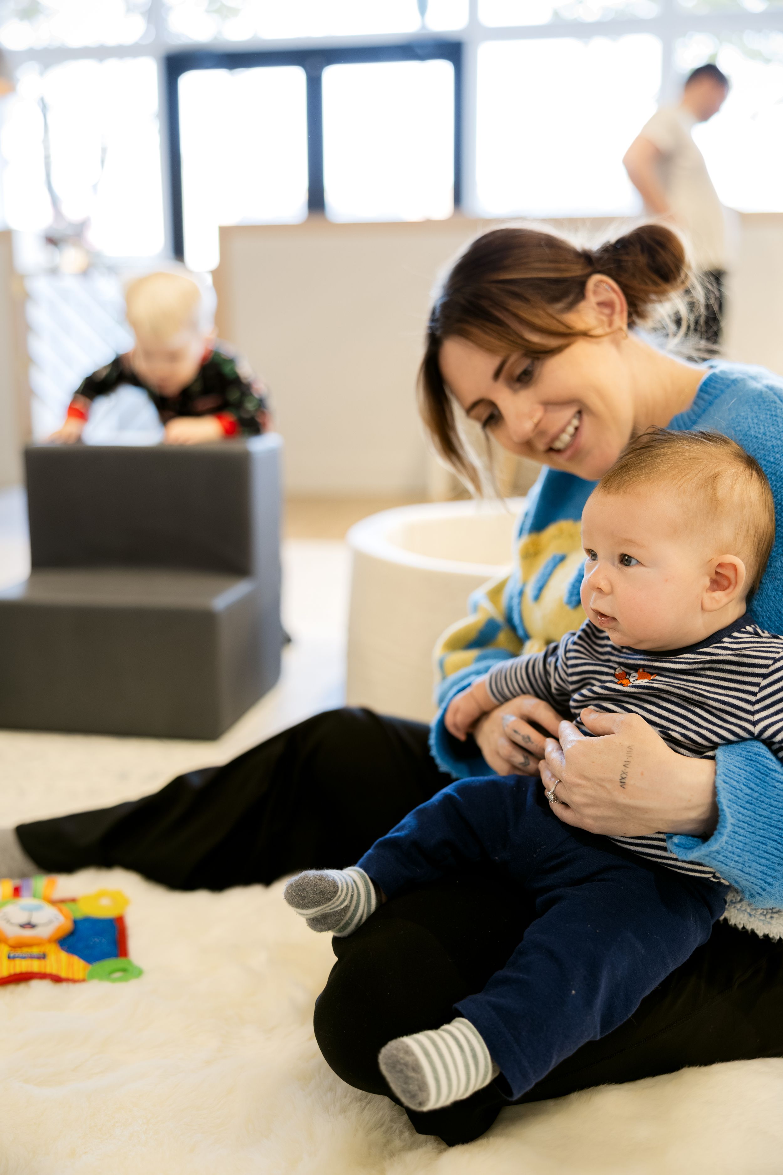 Baby in striped shirt plays and laughs while lying on floor in bright indoor space.