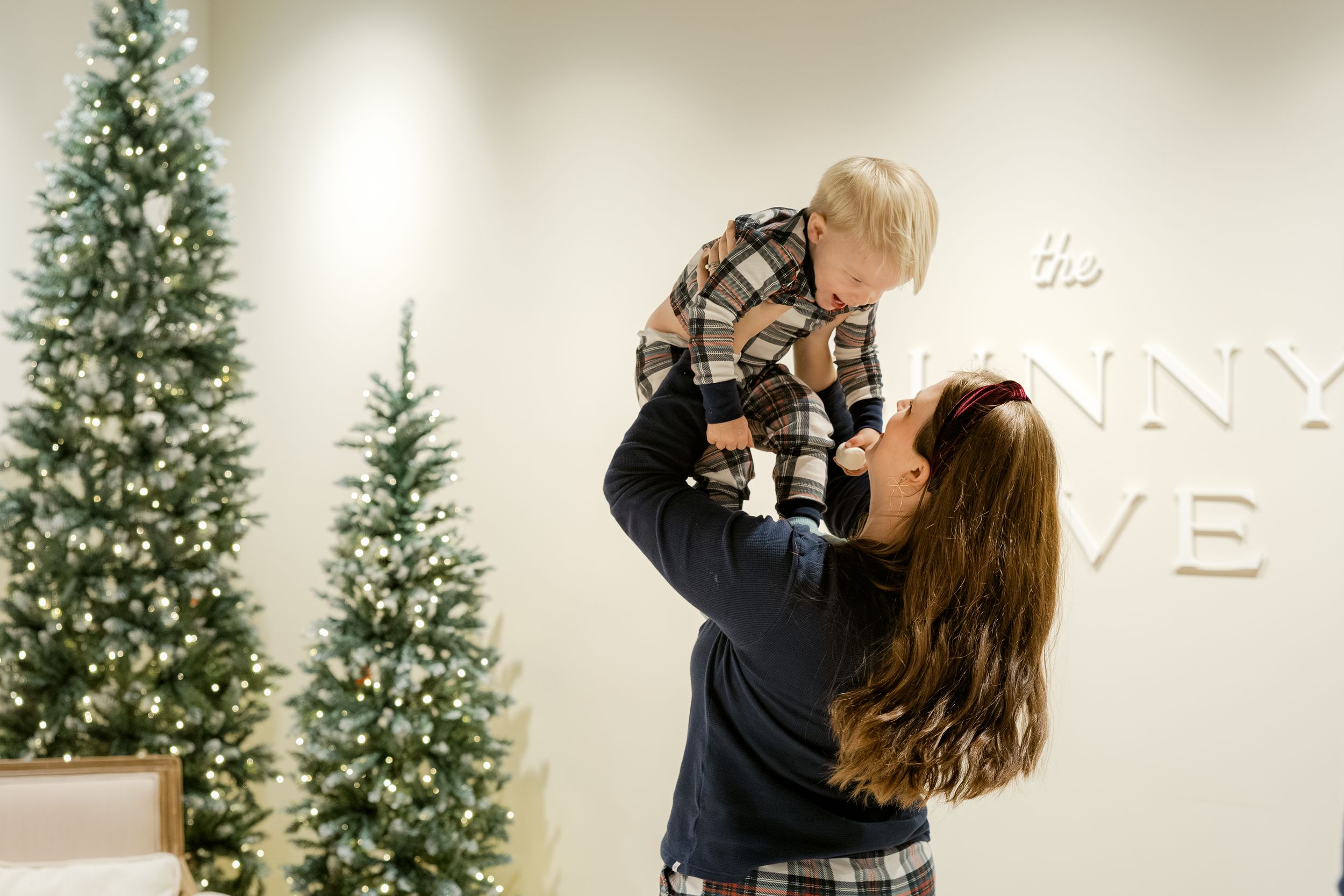 A couple shares a romantic kiss in front of a decorated Christmas tree in a modern indoor setting.