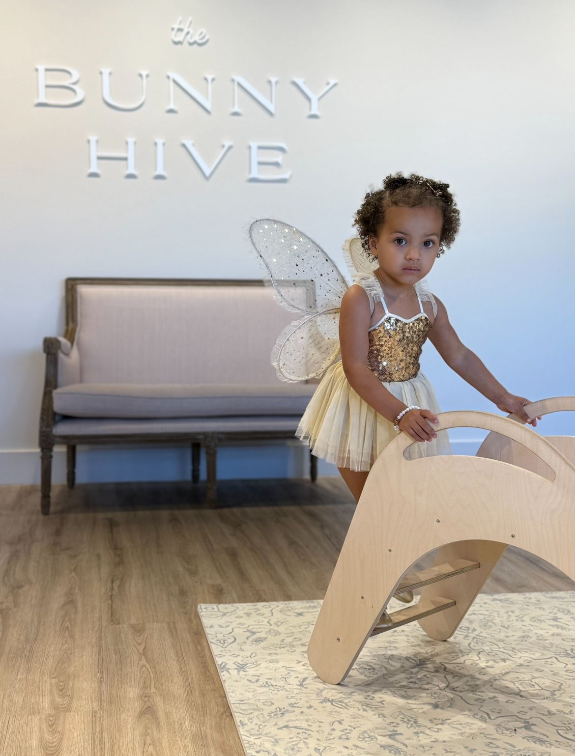 A small child plays with a wooden rocking toy on a light-colored carpet in a minimalist room setting.