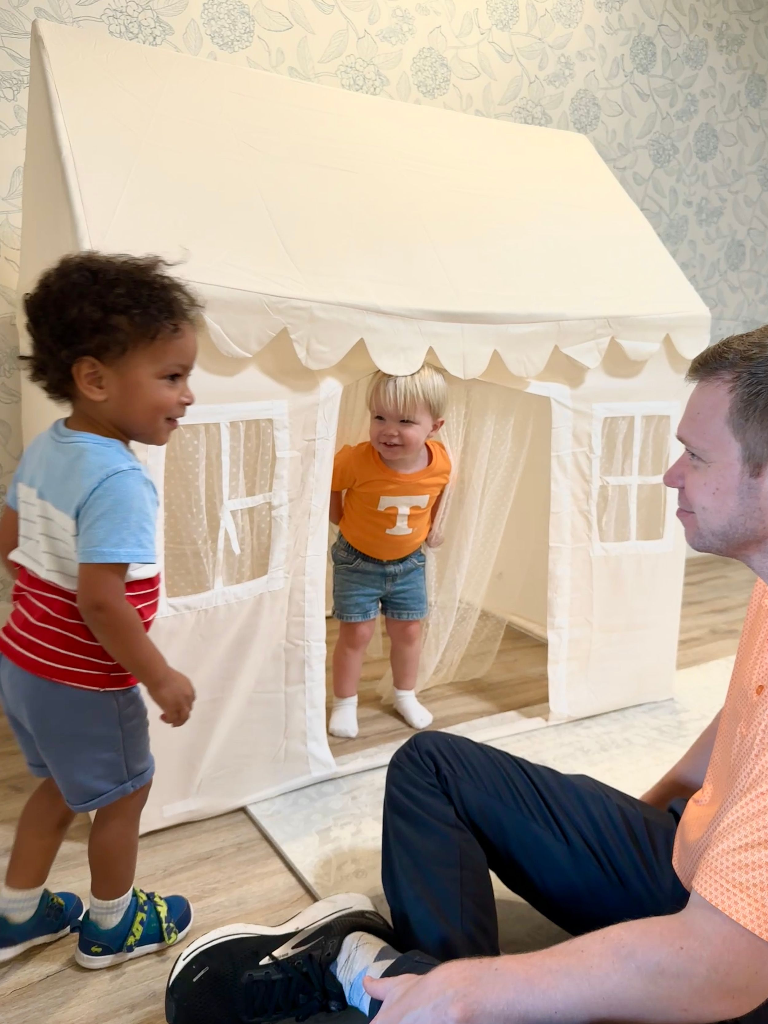 Young children explore and play in a white fabric tent structure with window cutouts in a sequence of candid moments.