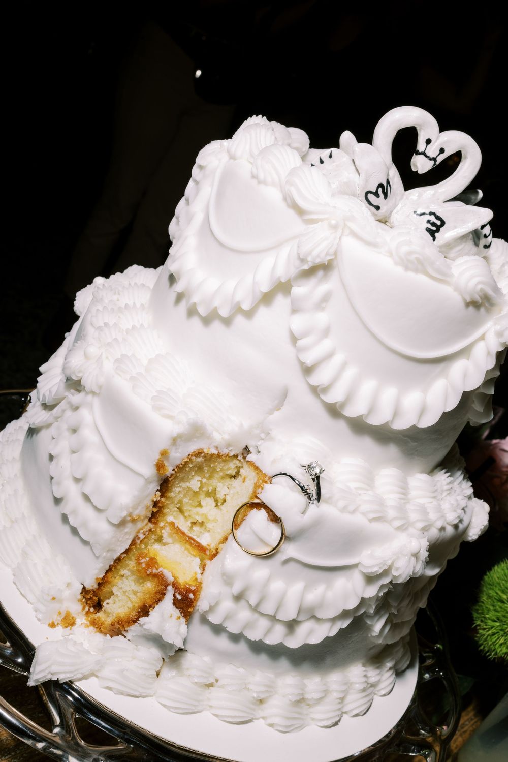 White wedding cake with intricate piped frosting details and decorative swirls on a dark background.
