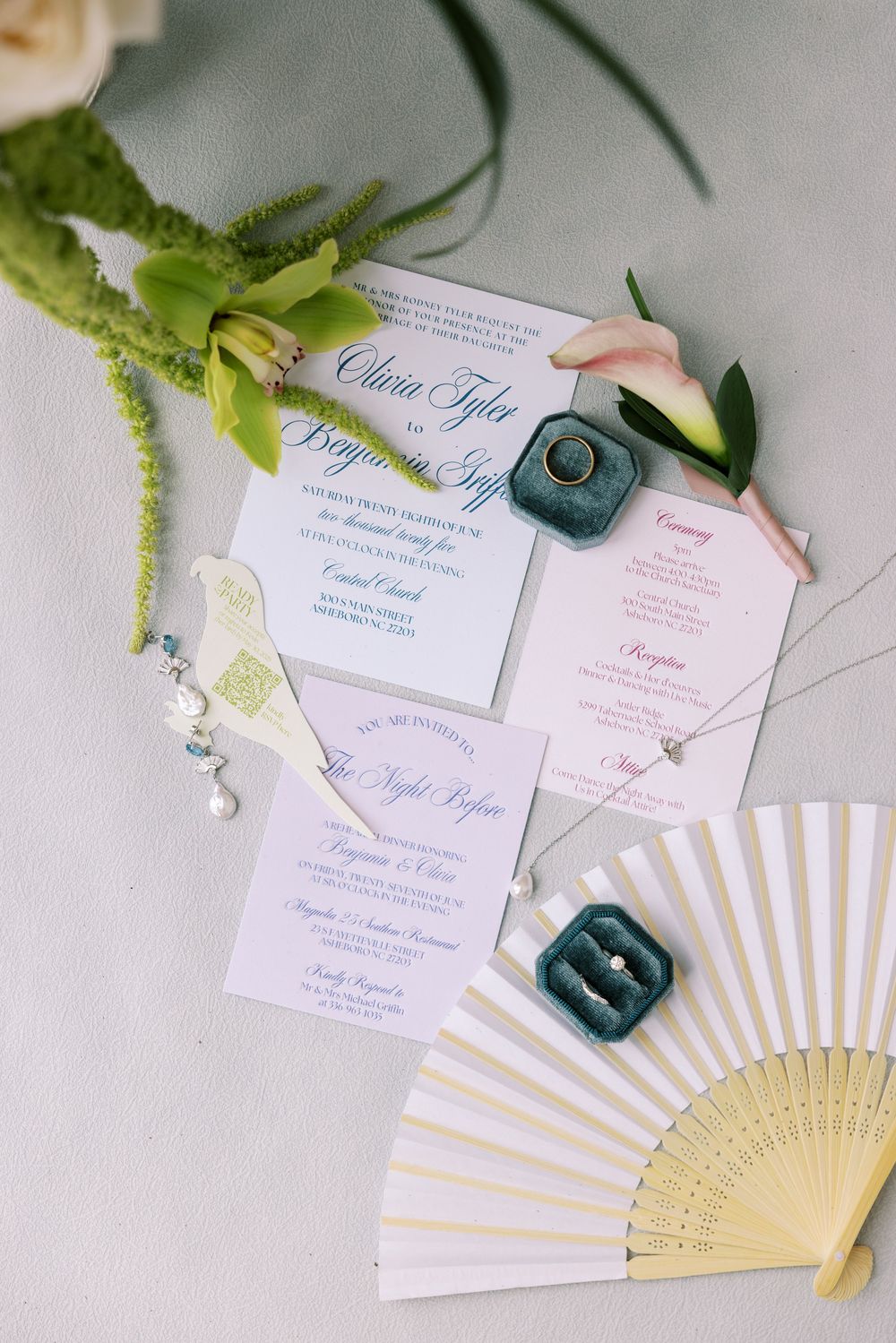 Wedding invitations and paper fans arranged with greenery on a light surface.