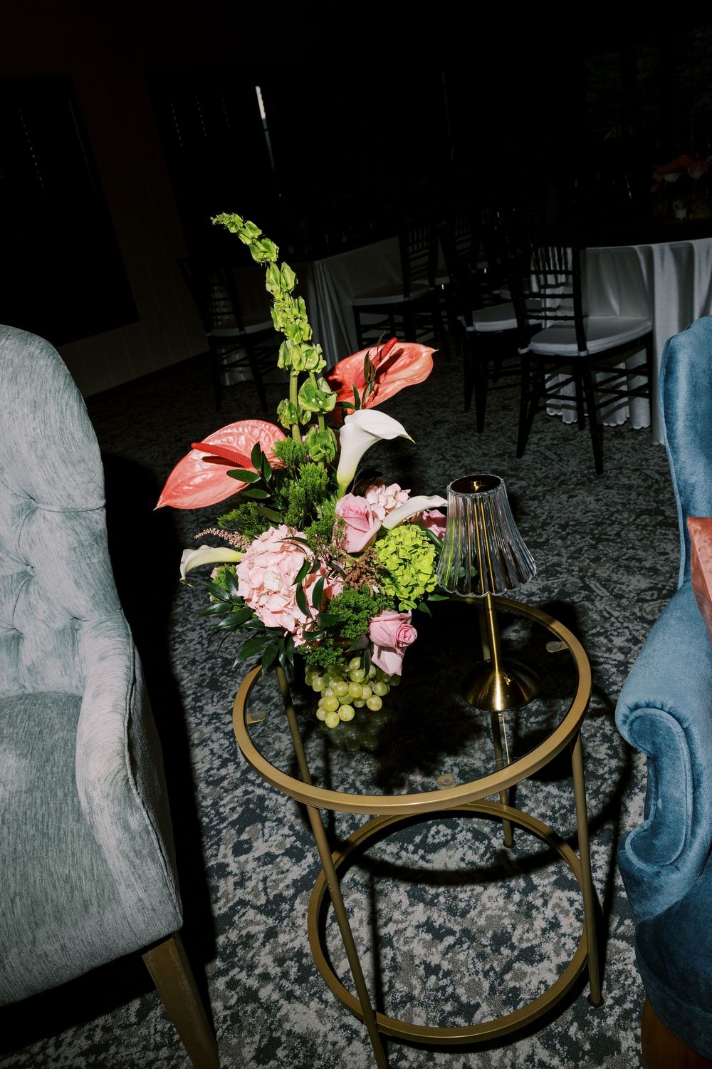 Floral centerpiece with pink anthurium and greenery on a mirrored table surface.