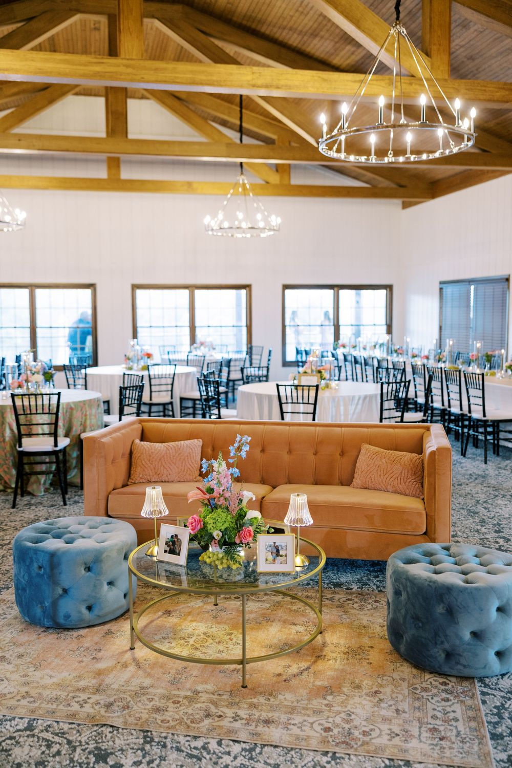 Wedding venue lounge area with tufted blue ottomans and tan couch under wooden beam ceiling.