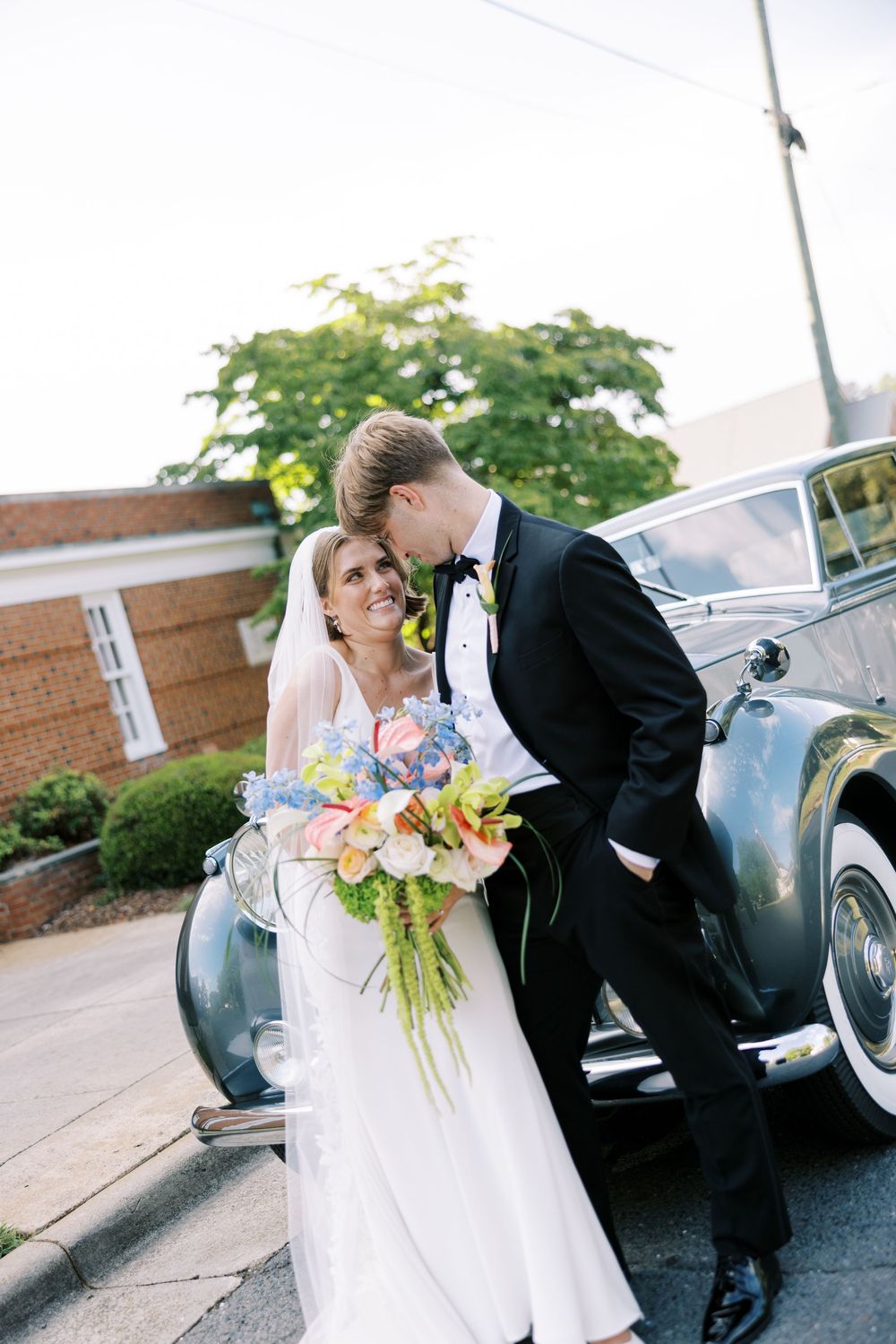 Classic black vintage car serves as backdrop for romantic wedding couple portraits.
