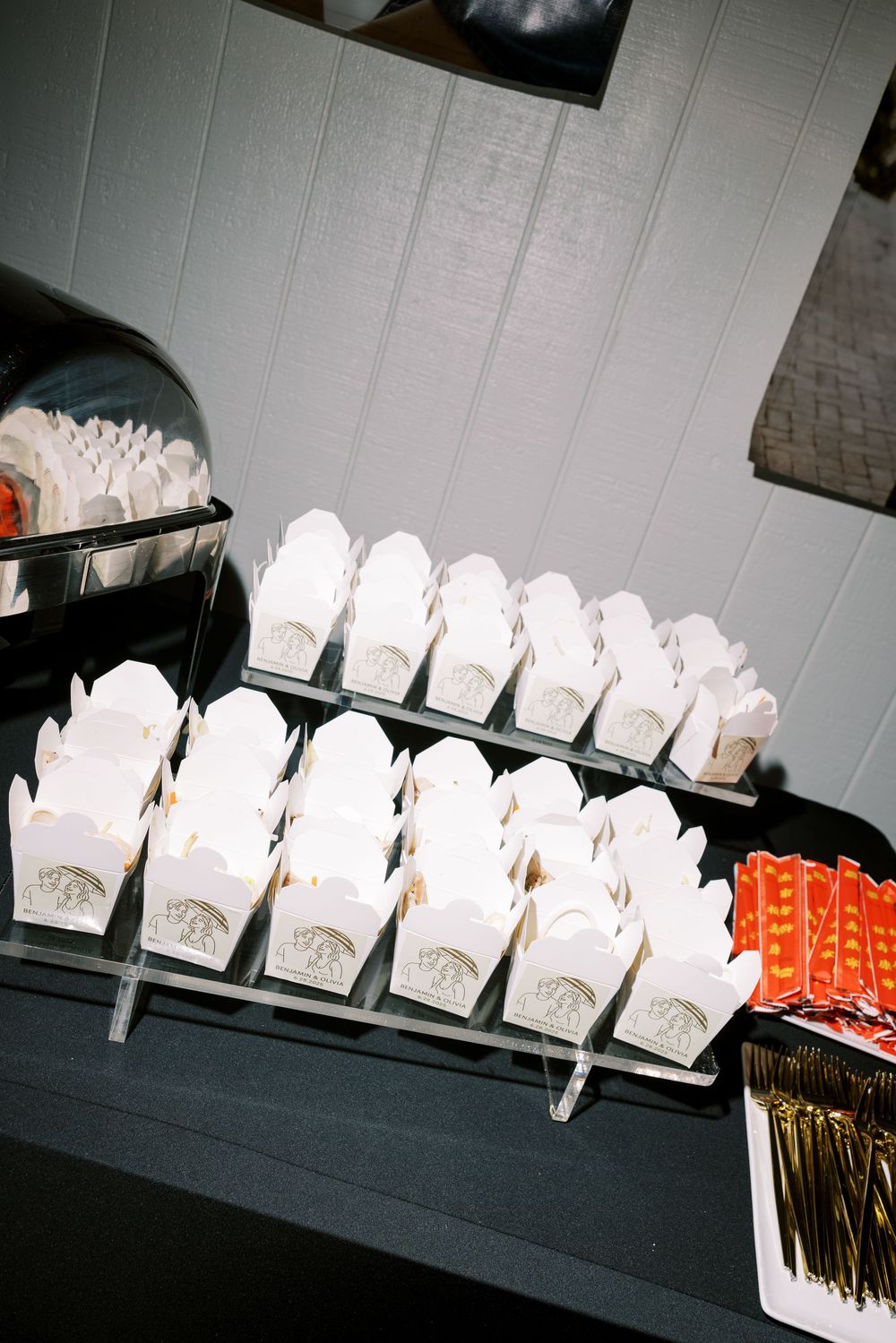 Rows of white takeout boxes arranged neatly on black shelving at a catering or food service event.
