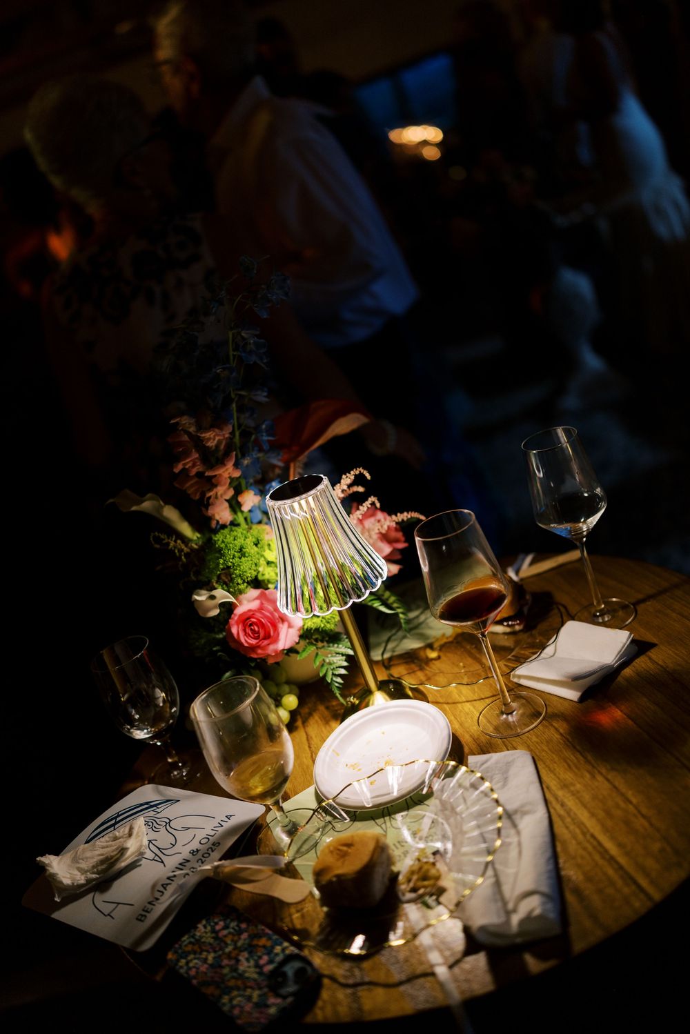 Moody table setting with wine glasses, a red rose, and decorative lamp casting dramatic shadows.