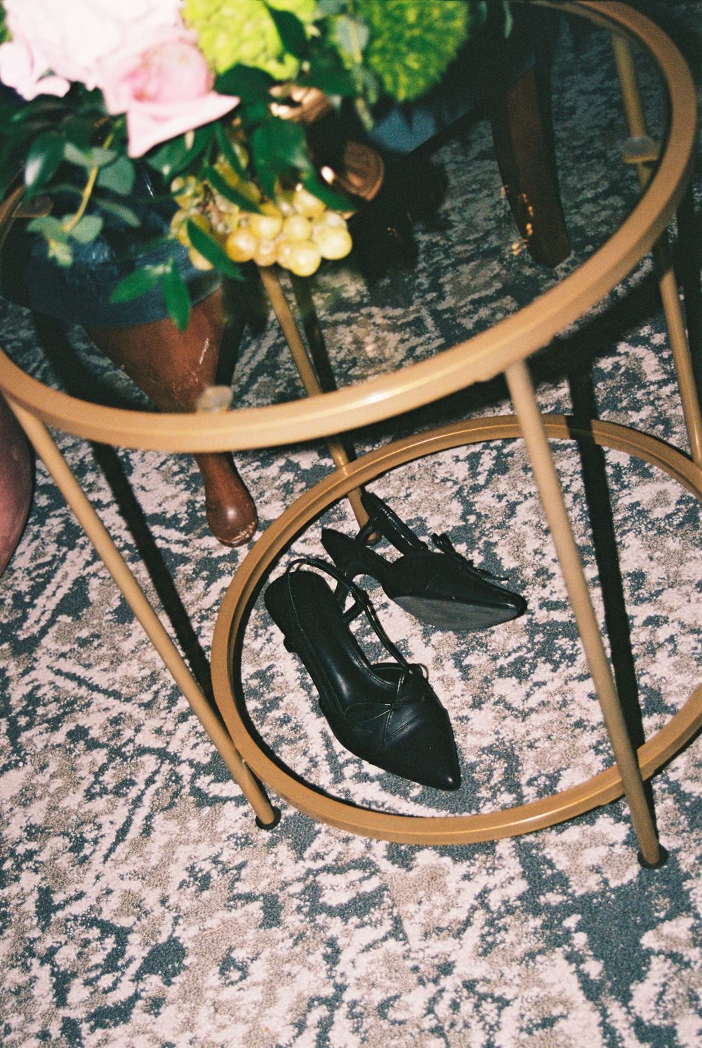 A pair of black leather shoes beneath a vintage brass side table with flowers on top.