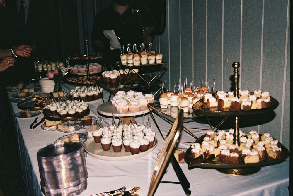 A dimly lit dessert table displays an elegant spread of cupcakes and sweet treats on tiered platters at an evening event.