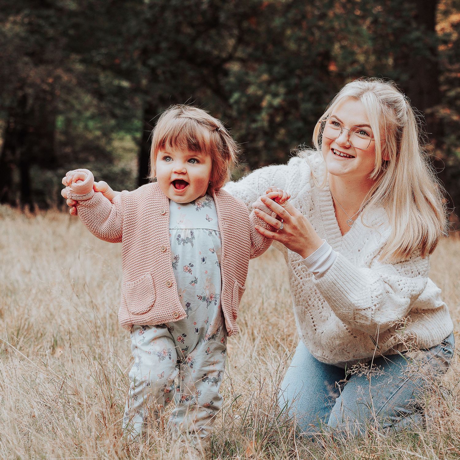 Mummy and Me photo of a young girl taking her first steps through a meadow with her mum helping her.