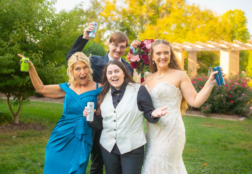 A group poses joyfully together outdoors with vibrant yellow autumn foliage in the background. Quad Cities Wedding Photography