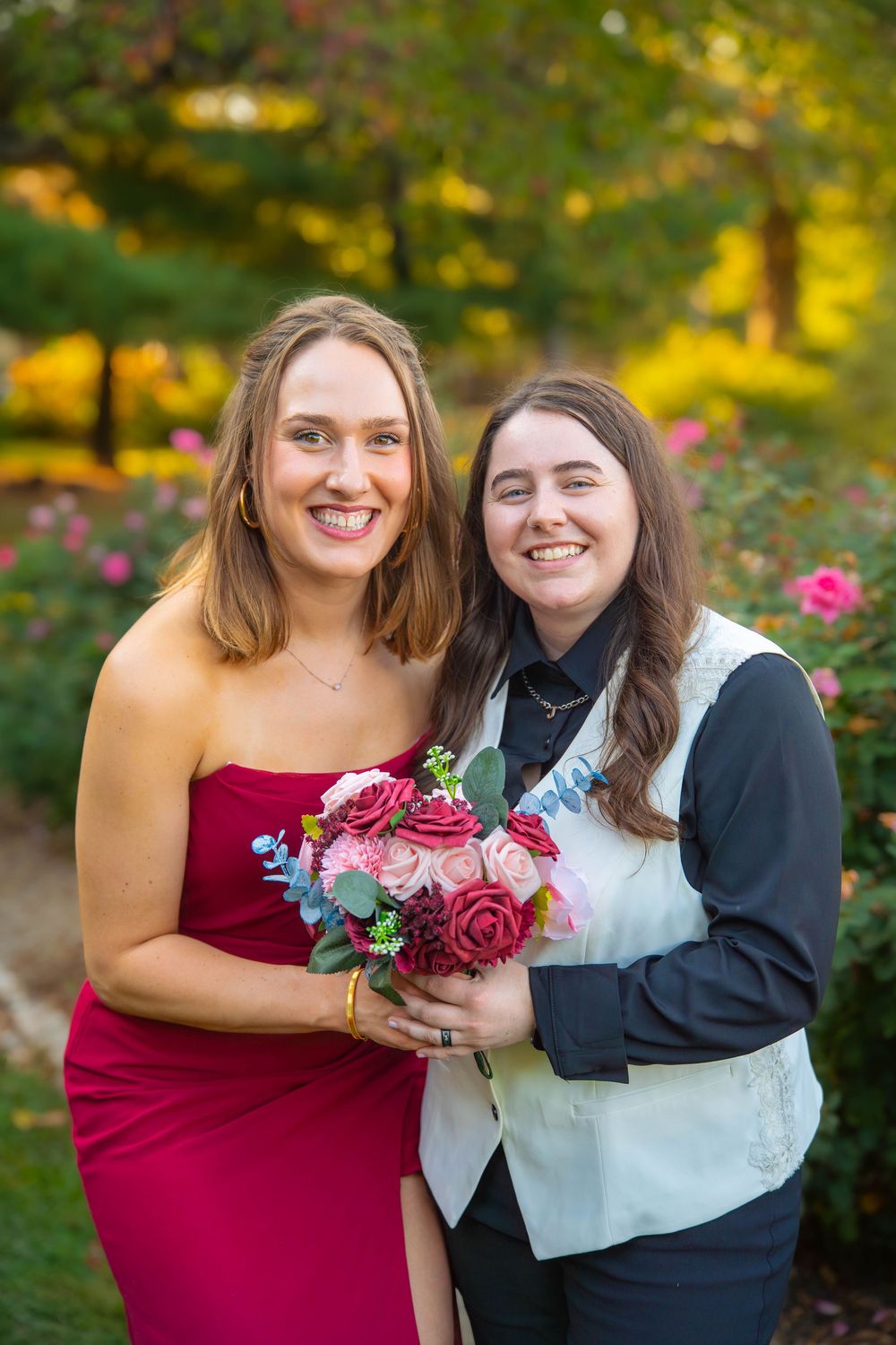 A couple in formal attire sharing joyful moments in a garden setting with burgundy flowers and autumn foliage.