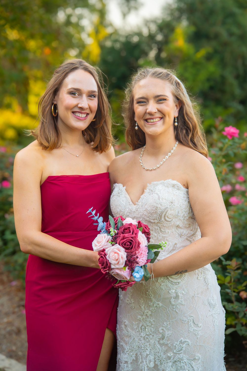Wedding party members in burgundy and white dresses pose together with bouquets in a garden setting.