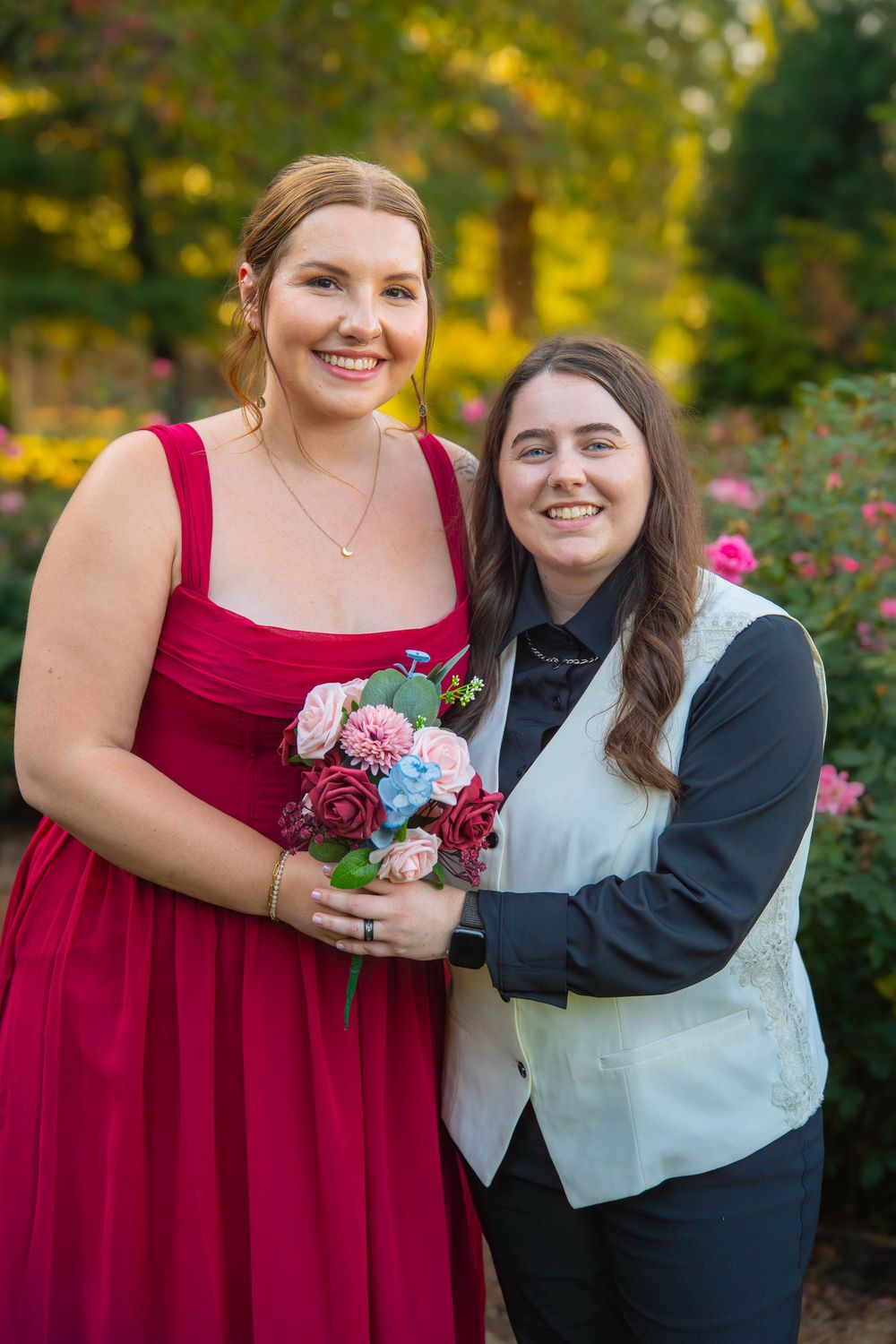 A couple poses together in a garden setting wearing burgundy and light colored formal attire.