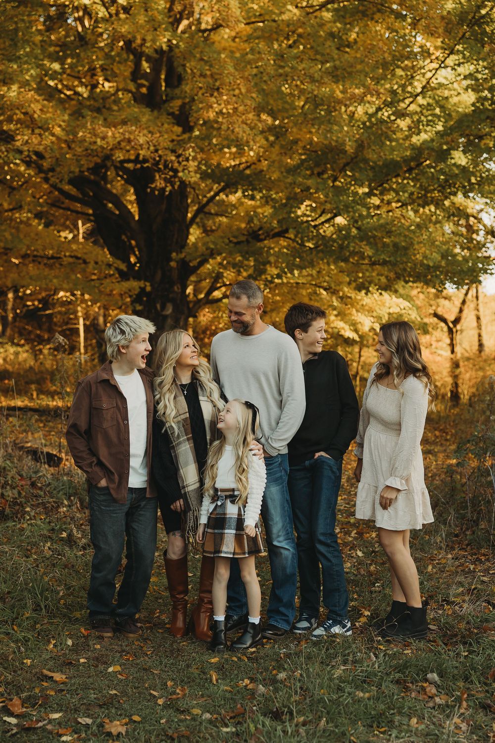 A group stands together under golden autumn trees during a fall photo session at sunset.