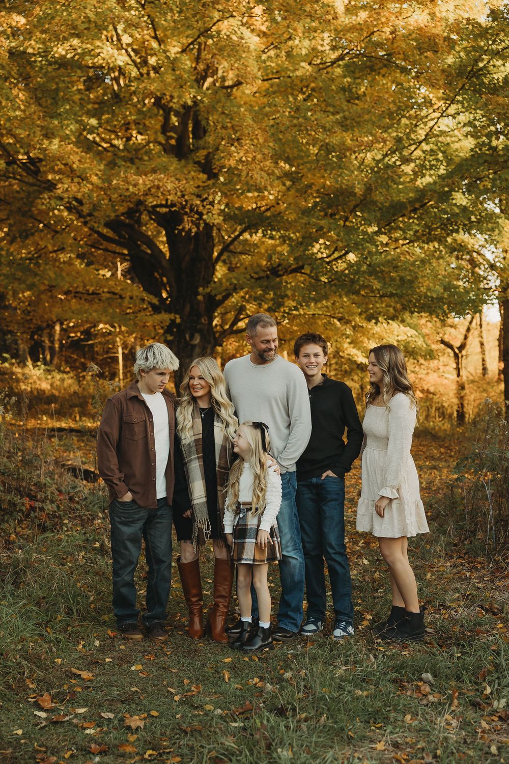 Group of people gathered under golden autumn trees at sunset in a park setting.