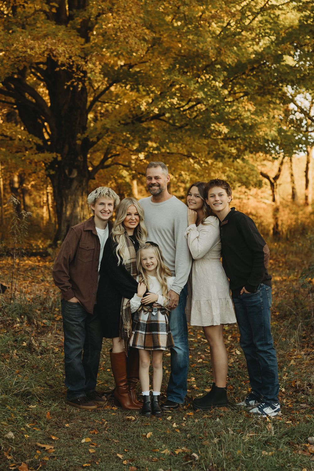 A group poses together outdoors in autumn with golden fall foliage and trees creating a warm seasonal backdrop.