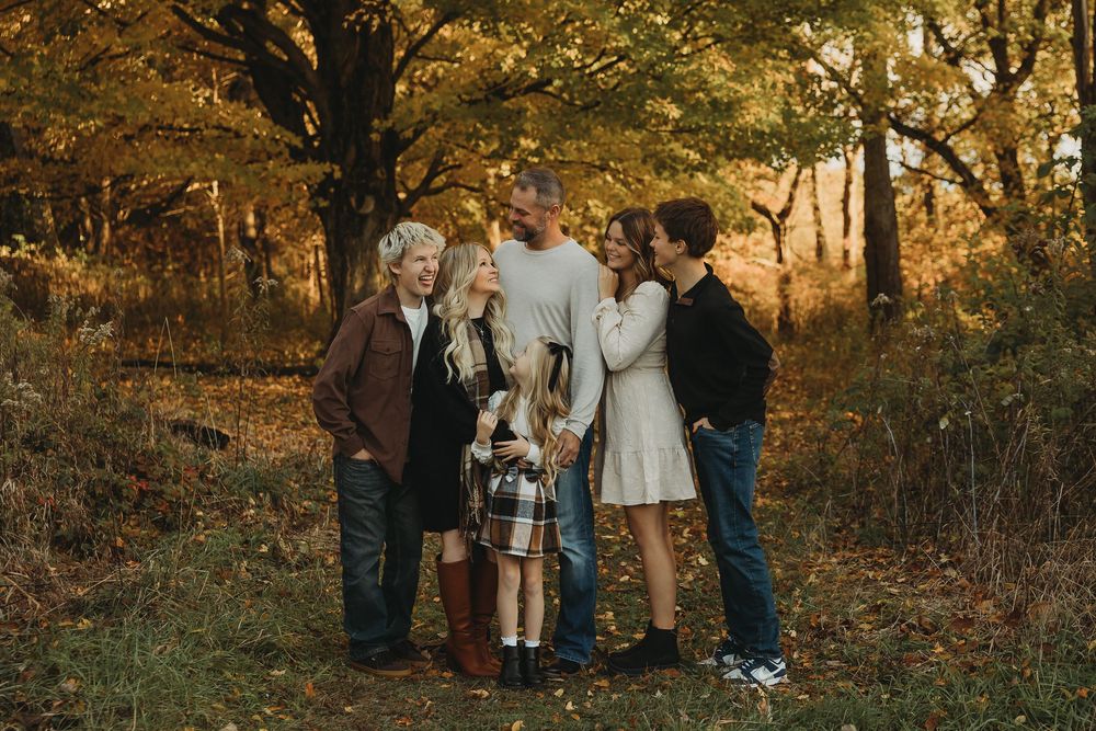 A group of people gather in a wooded area during golden hour with autumn foliage in the background.