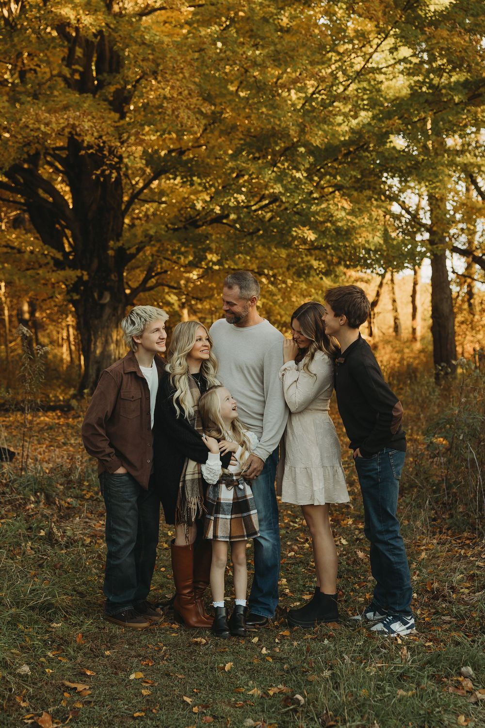 A group of people gather together in an autumn forest setting with golden sunlight filtering through the trees.