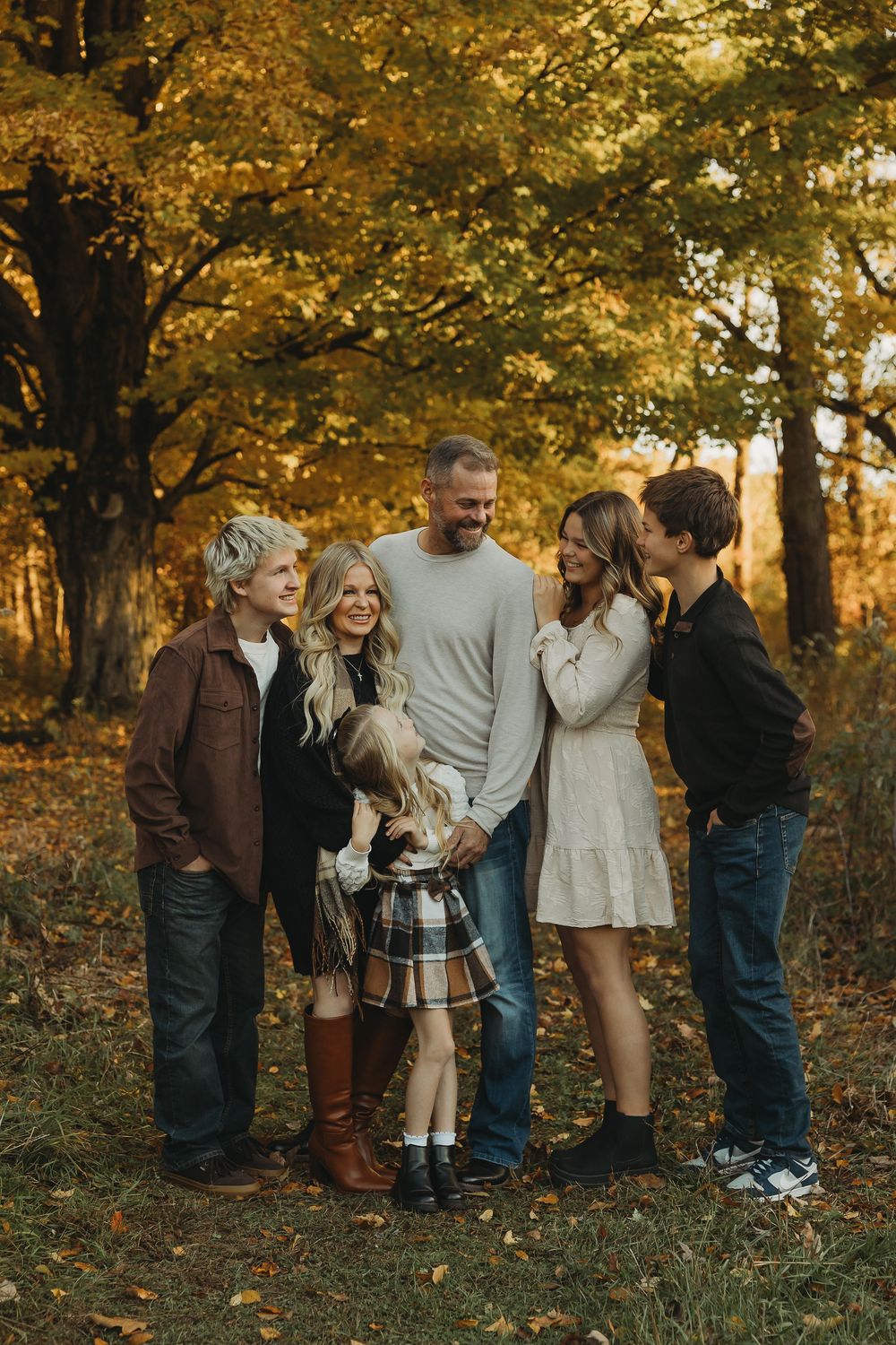A group stands together laughing and smiling among golden autumn trees in a forest setting.