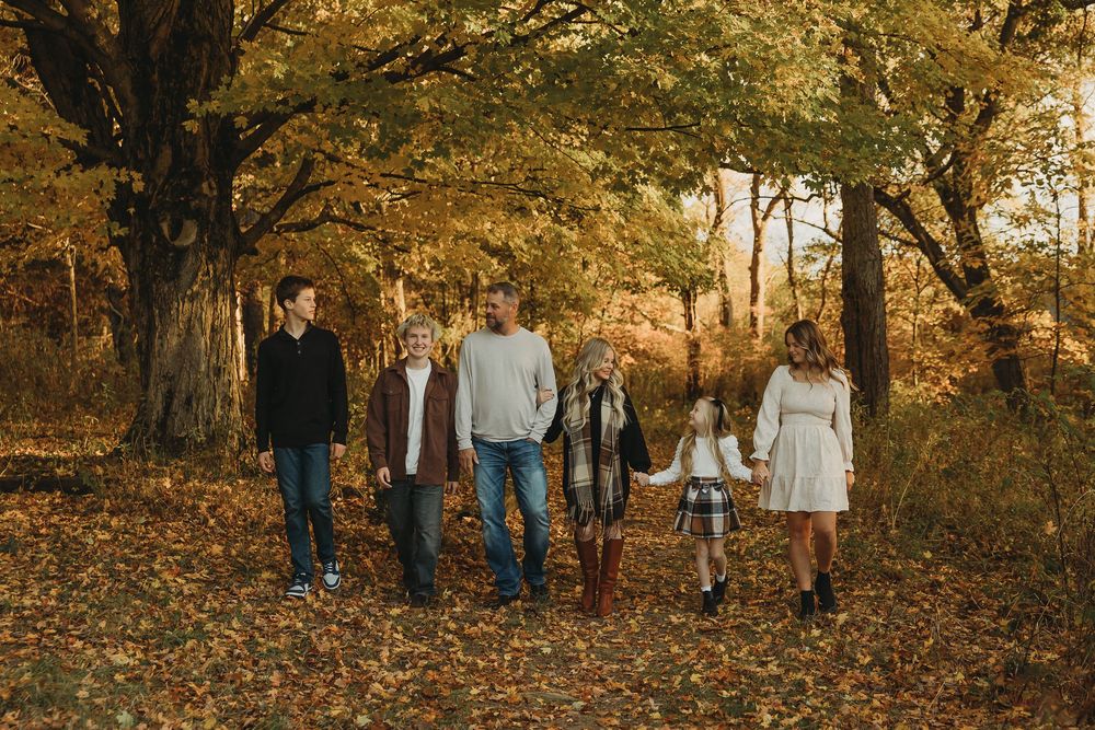 A group walks together through fallen leaves on an autumn forest path with golden trees overhead.