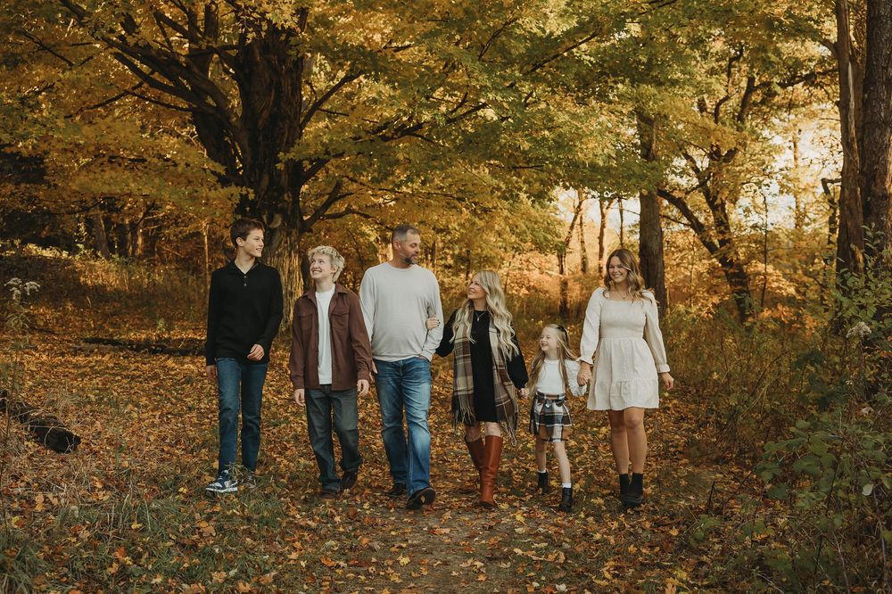 A group walks together through a wooded area with golden autumn foliage during sunset.