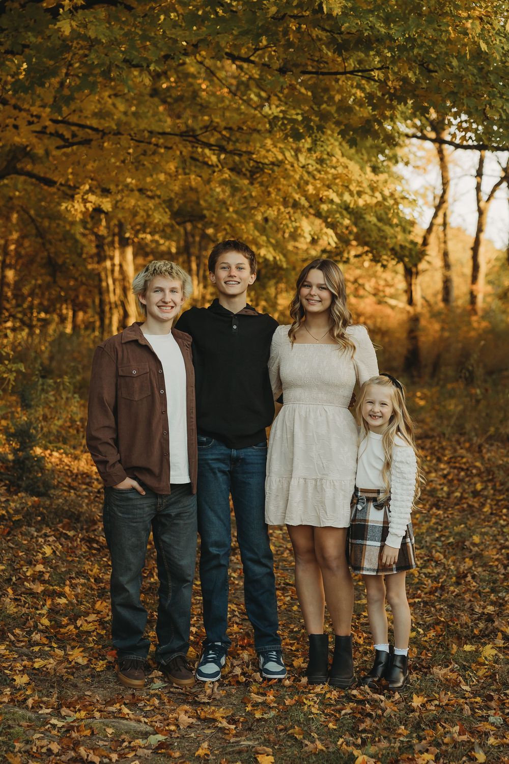 A family poses together in a fall forest setting with golden autumn leaves and warm sunlight filtering through the trees.