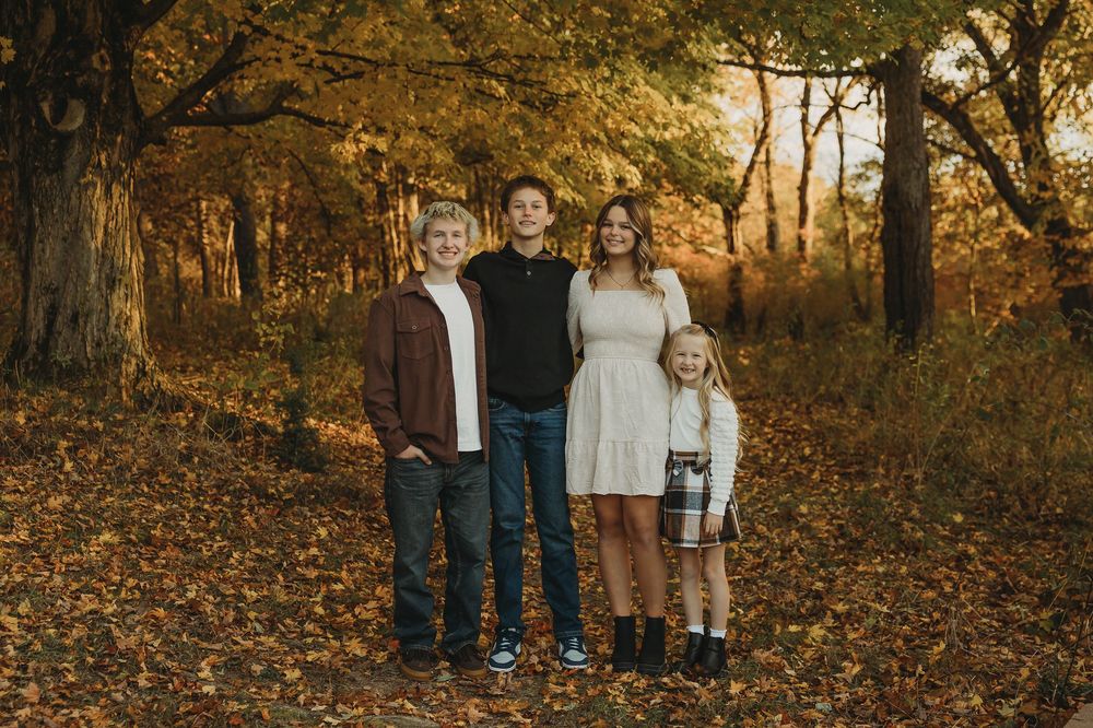 A family stands together in a golden autumn forest setting during a fall photography session at sunset.