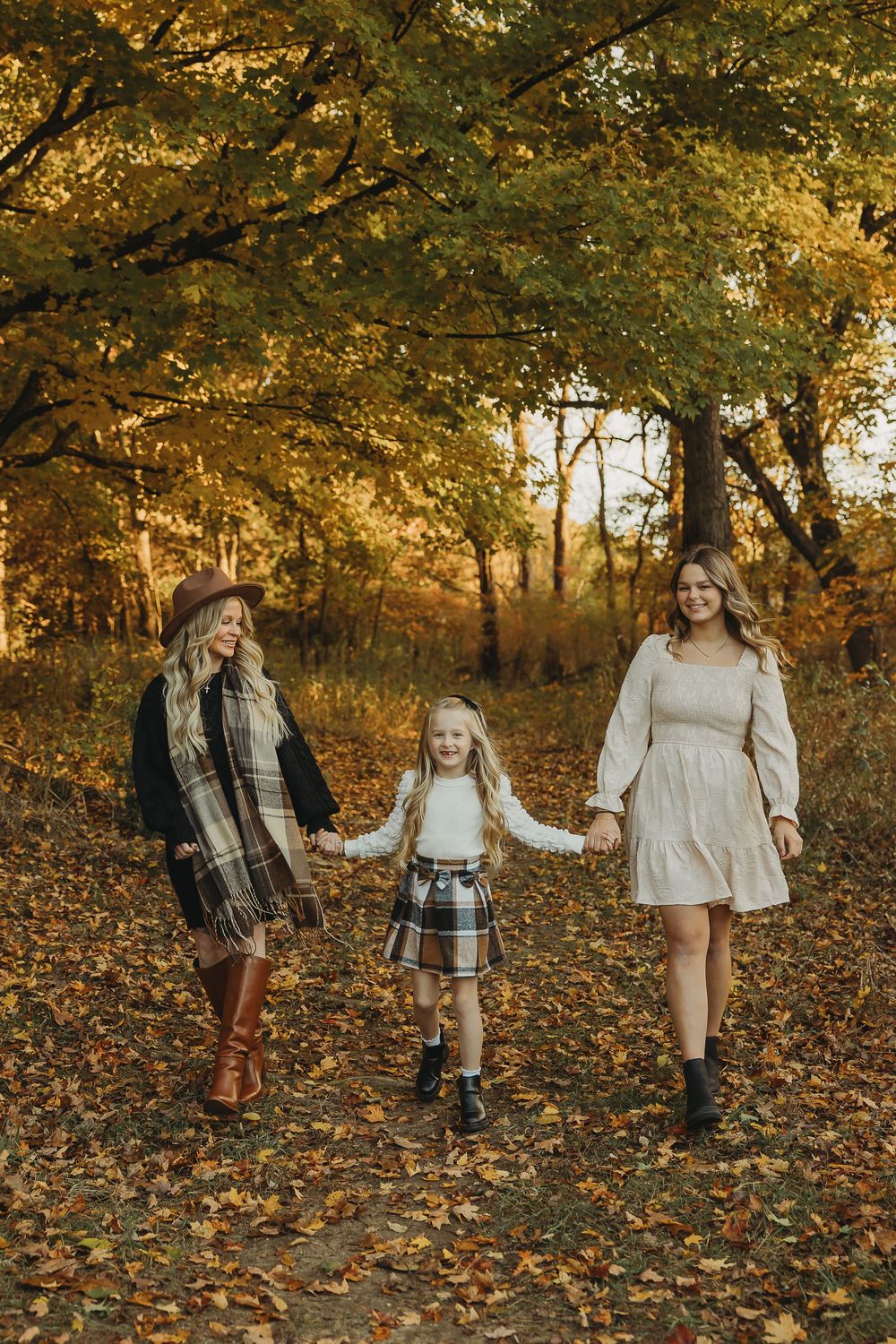 A group walks together through a forest path covered in golden autumn leaves during a fall photo session.
