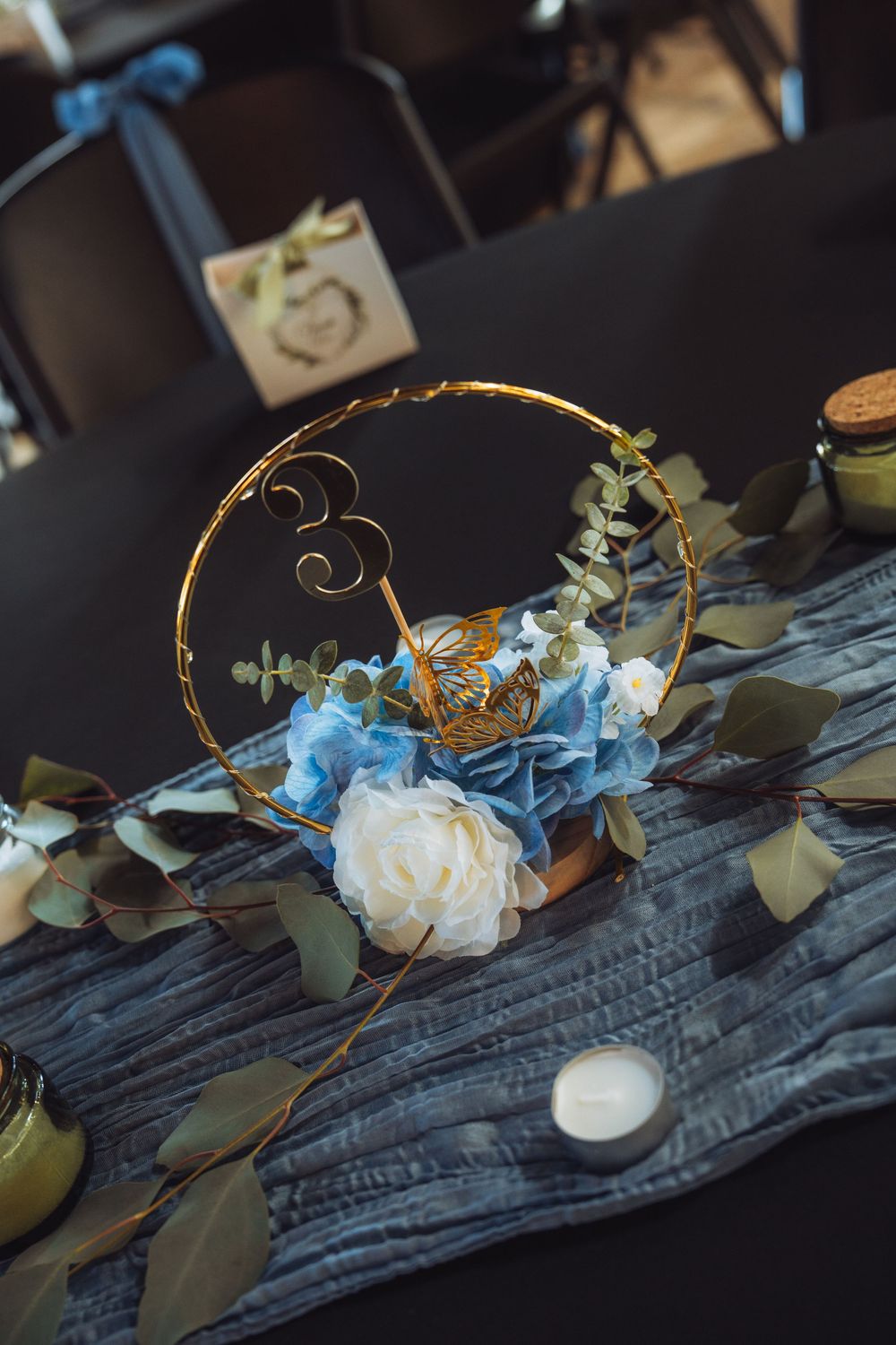 Wedding table centerpiece with blue and white flowers, greenery and twisting gold accents.