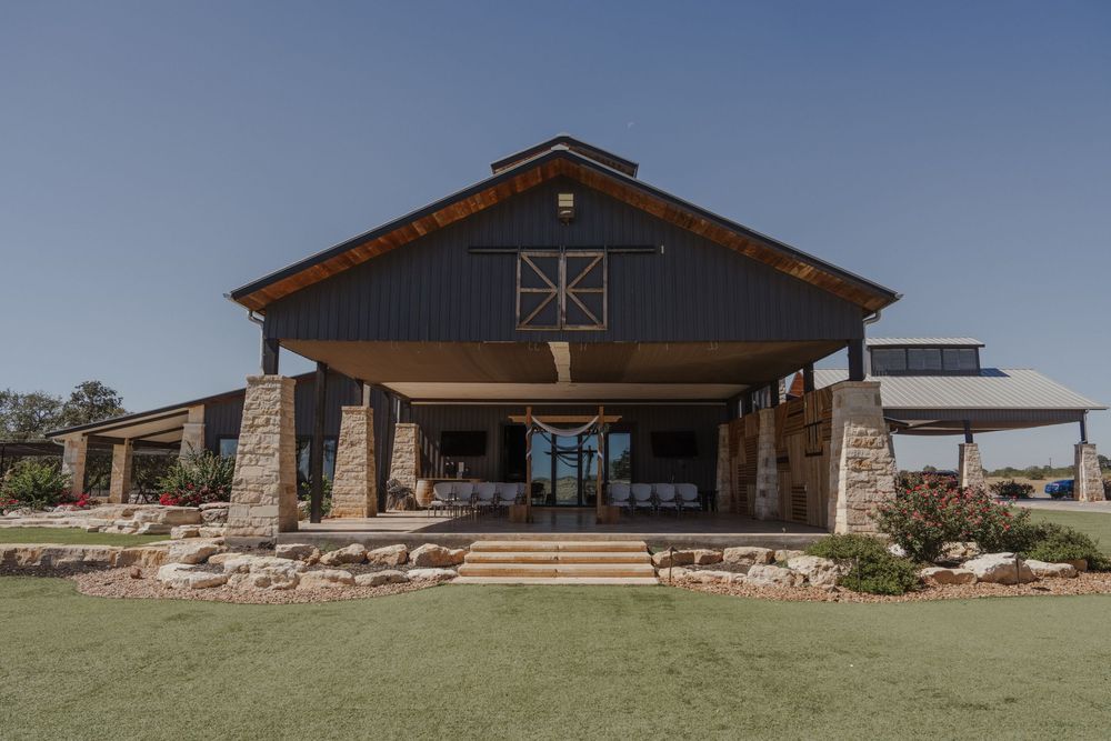Modern rustic event venue with stone and wood exterior set against clear blue sky.