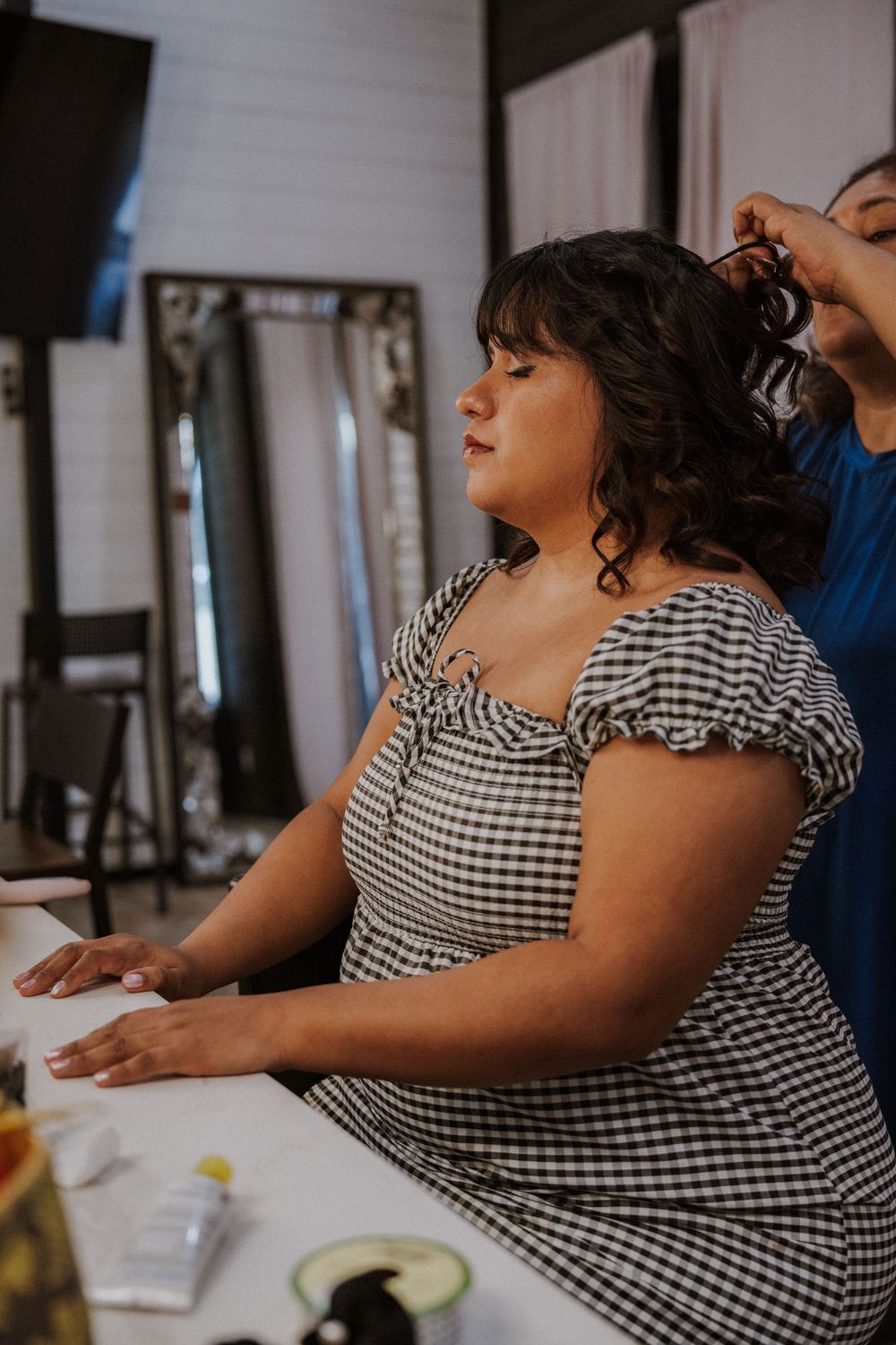Someone in a checkered dress sits at a table during what appears to be a wedding preparation moment.