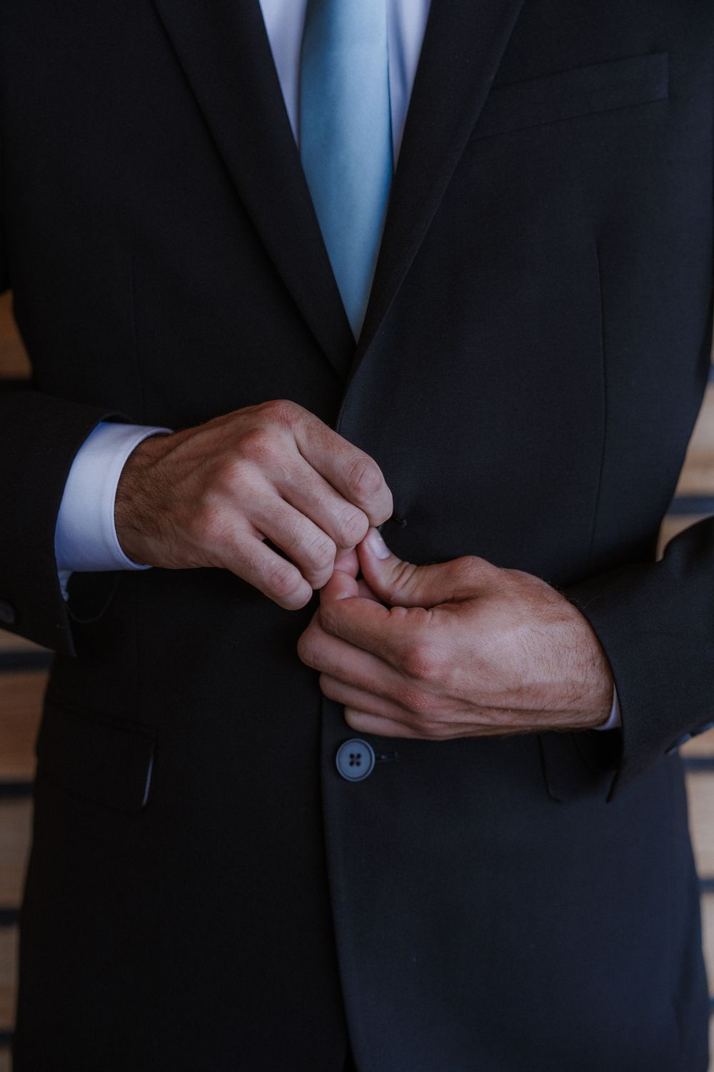 Close-up of hands in a navy suit adjusting cufflinks before the ceremony.