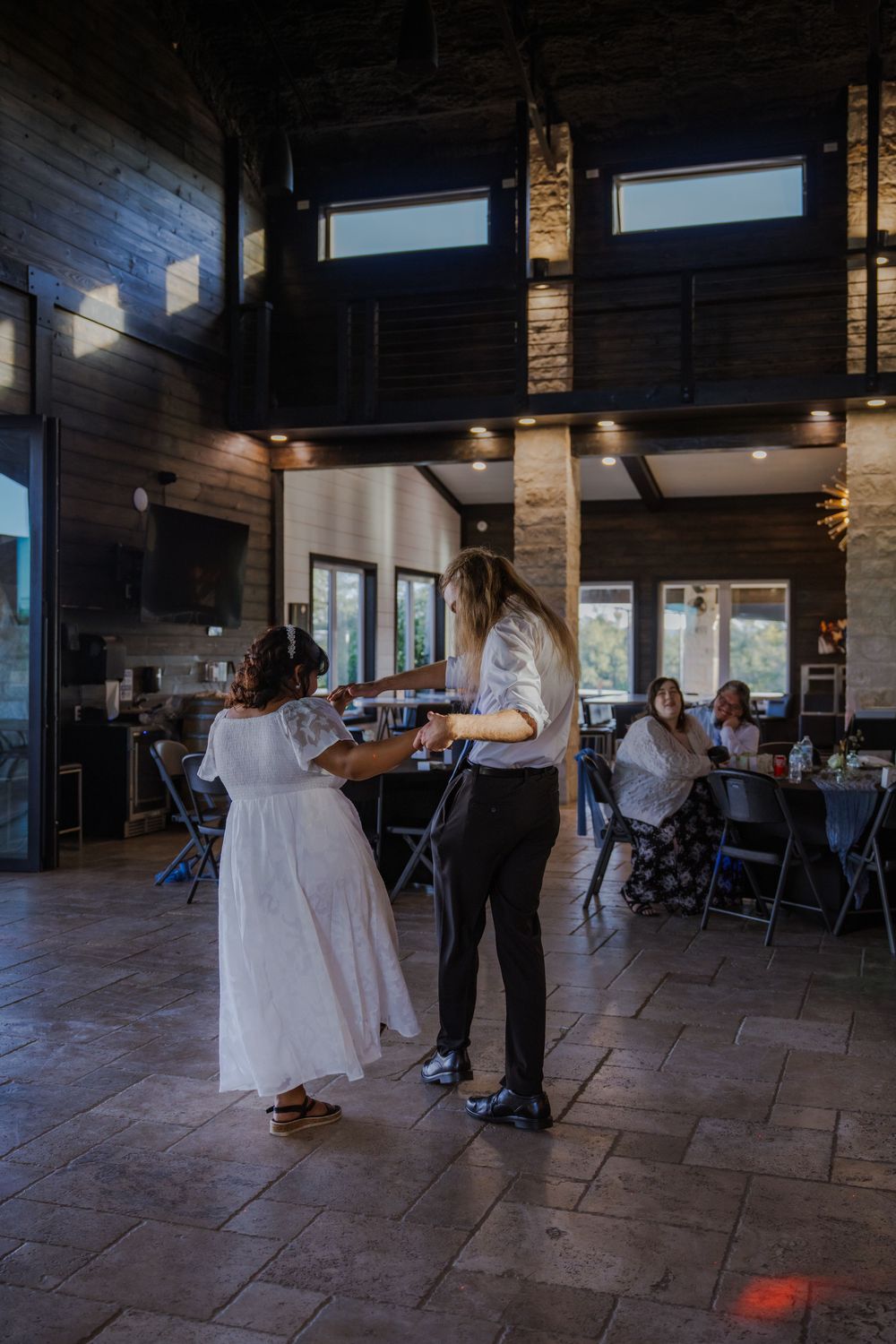 Wedding couple dancing in spacious indoor venue with stone pillars and tiled floor.