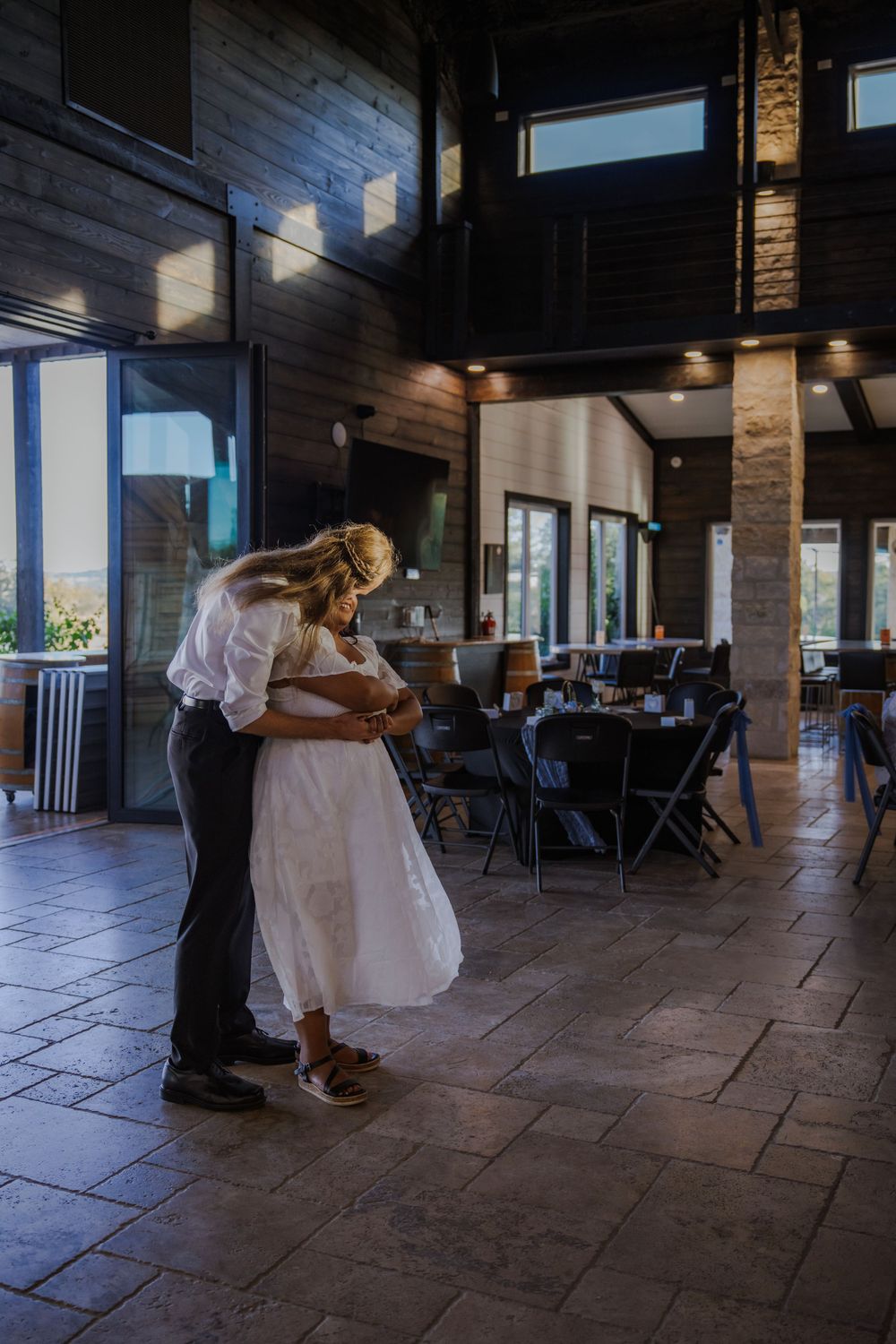 Couple sharing a dance moment in rustic indoor venue with natural lighting.