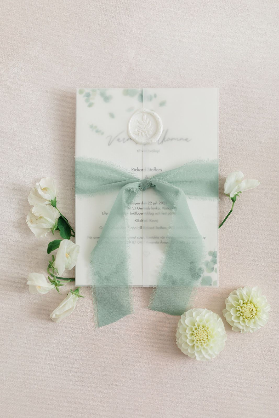 Elegant wedding invitation with mint green silk bow and white flowers arranged on light beige background.