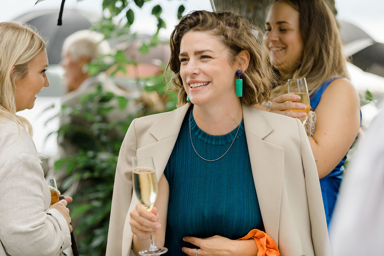 People enjoying drinks and conversation at an outdoor gathering, with someone wearing a beige blazer and teal top.