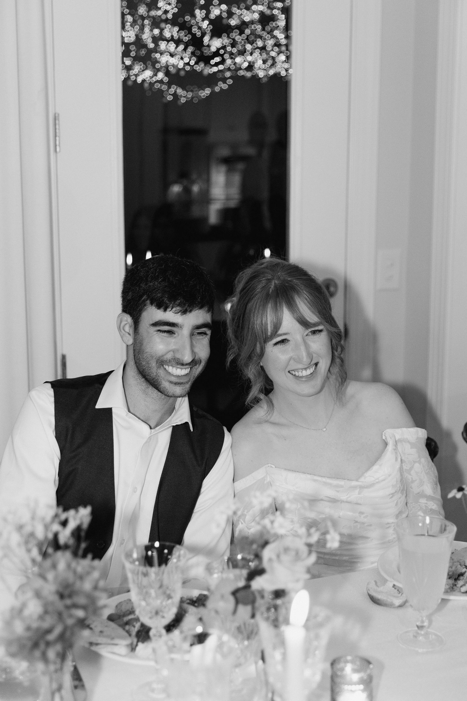 A black and white photo of a couple in wedding attire sharing a joyful moment at their reception table in Durham NC, documentary coverage